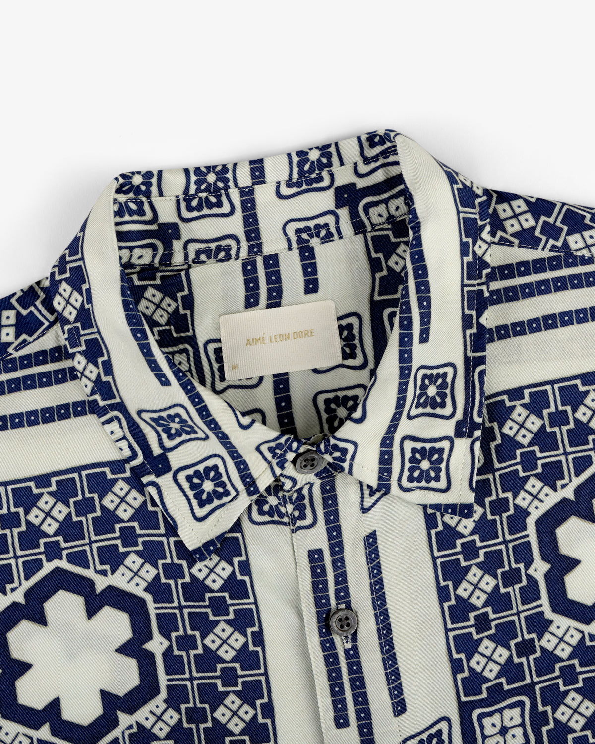 Close-up of the Mosaic Button Down Shirt with a blue and white geometric pattern and buttons, Aimé Leon Dore label inside.
