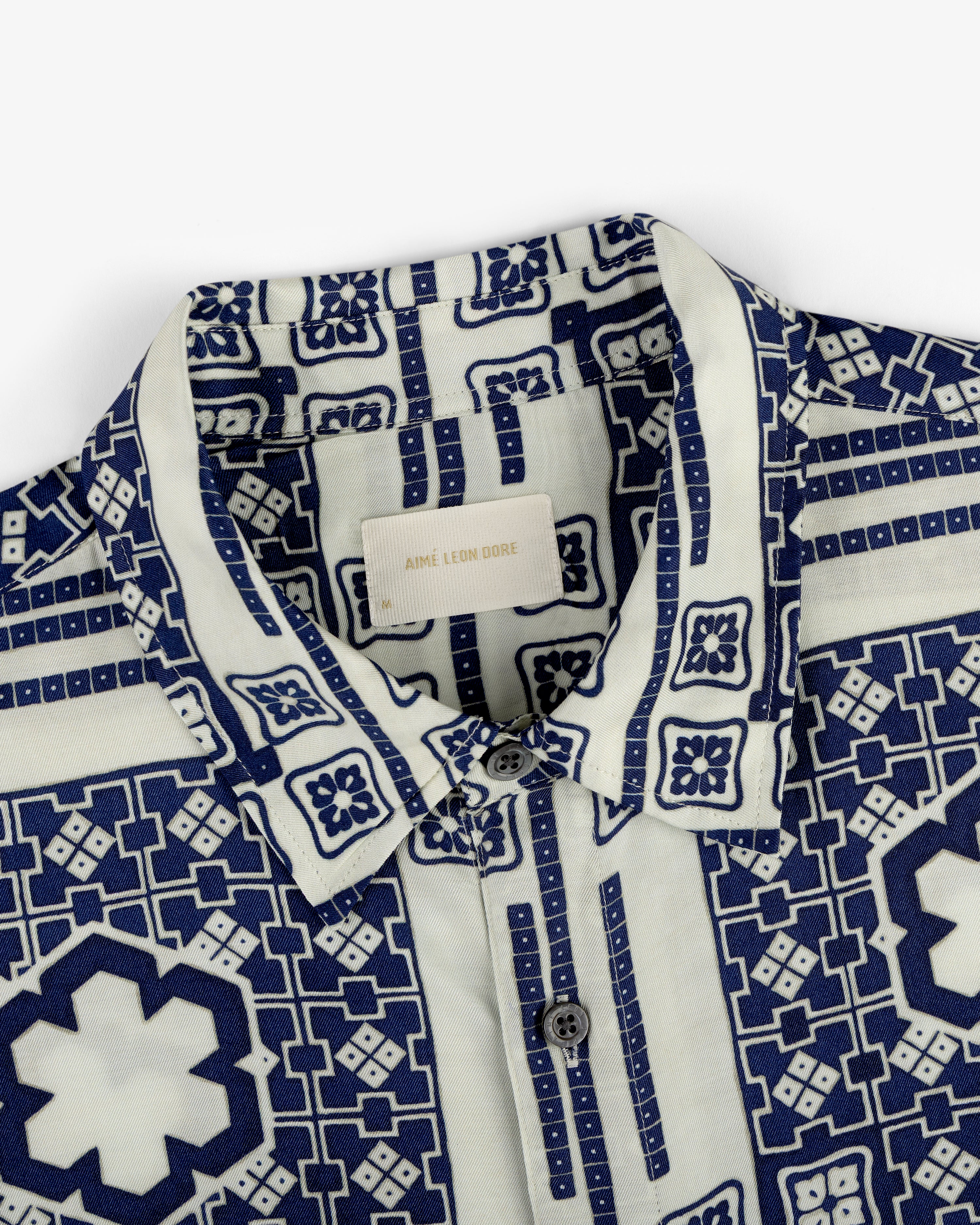 Close-up of the Mosaic Button Down Shirt with a blue and white geometric pattern and buttons, Aimé Leon Dore label inside.