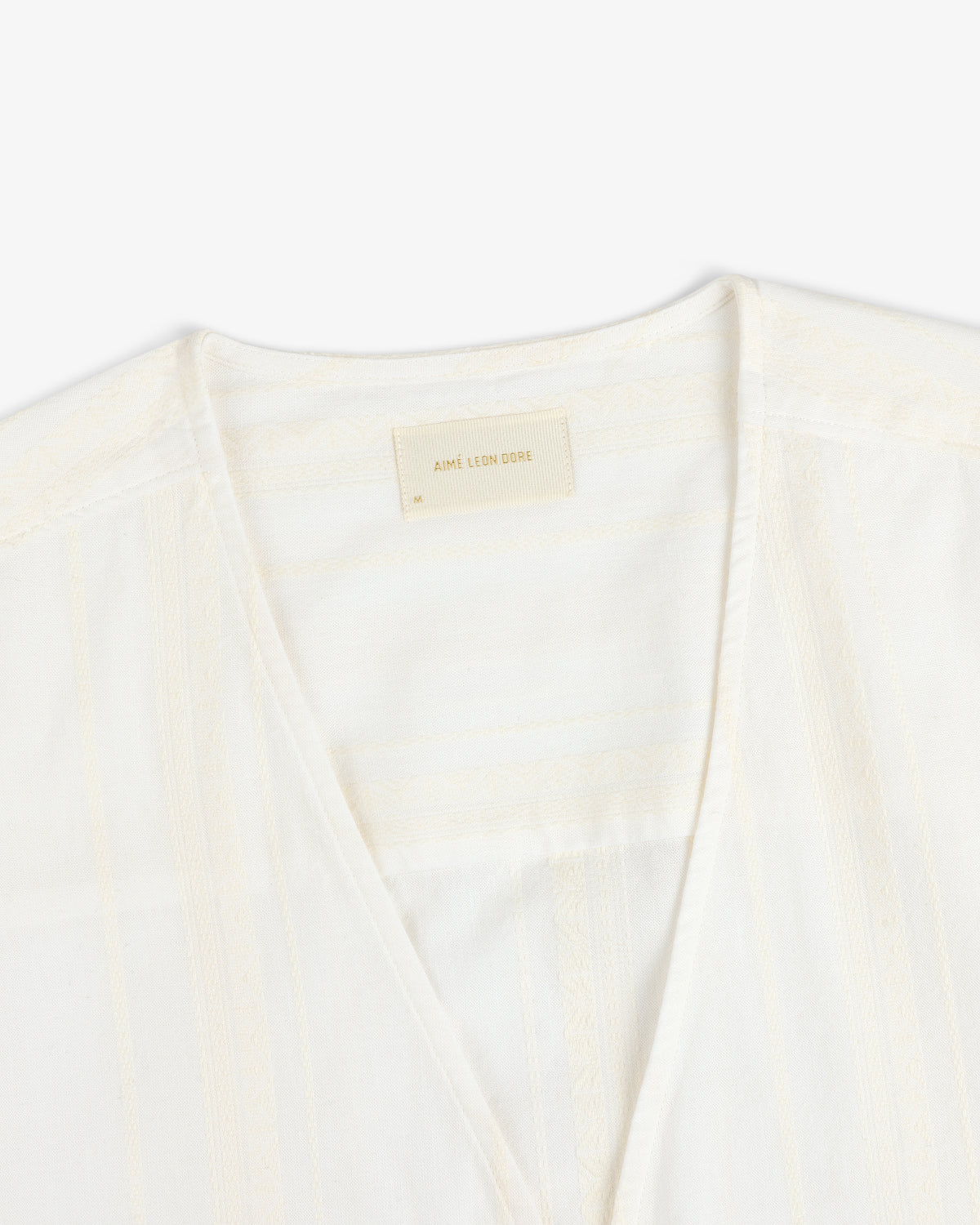 Close-up of the Jacquard Striped Tie-Front Shirt, cream-colored with subtle patterns and a beige Aimé Leon Dore label.