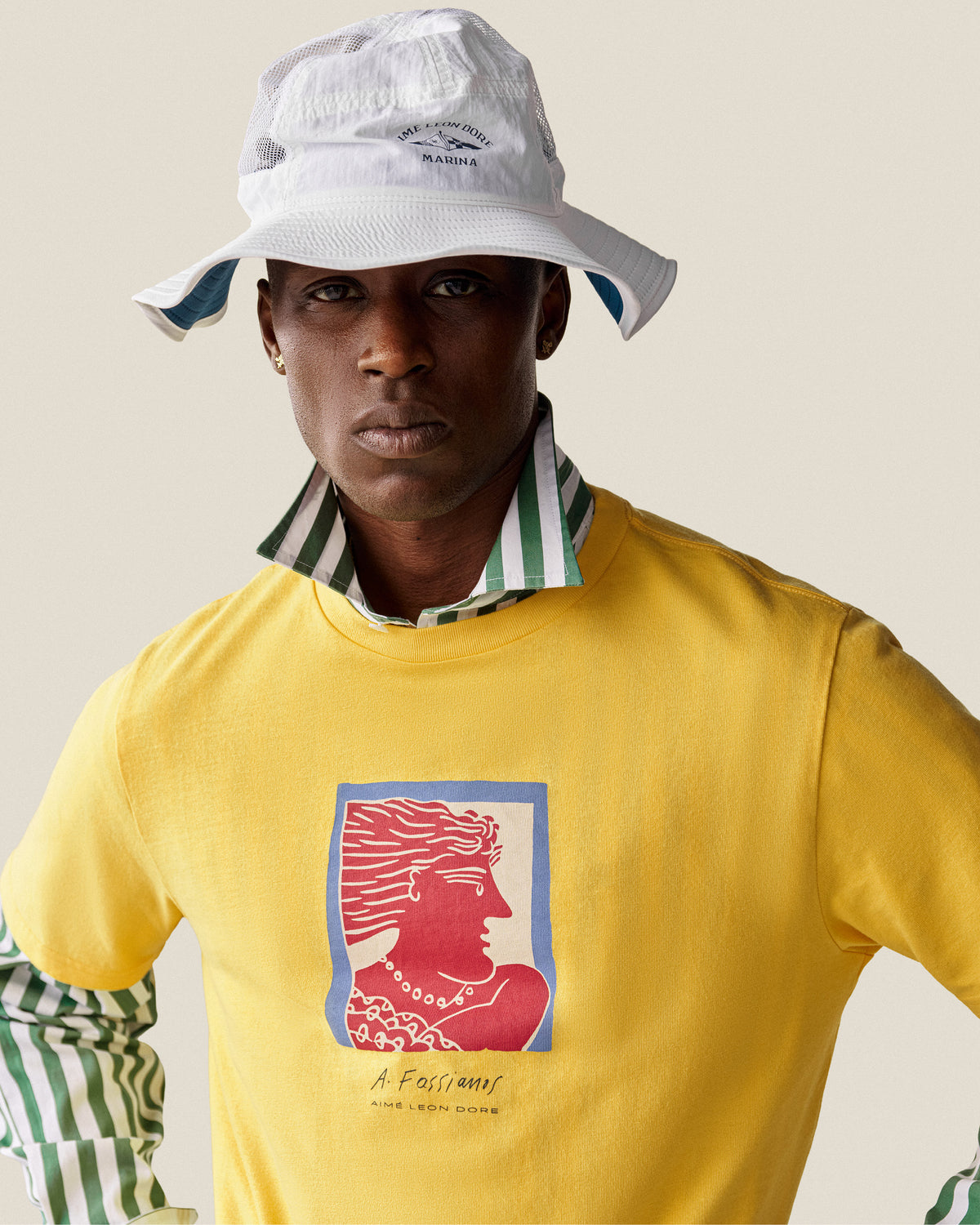 Man wearing a Marina Boonie Bucket Hat, yellow face print shirt, and green-striped collared shirt underneath.
