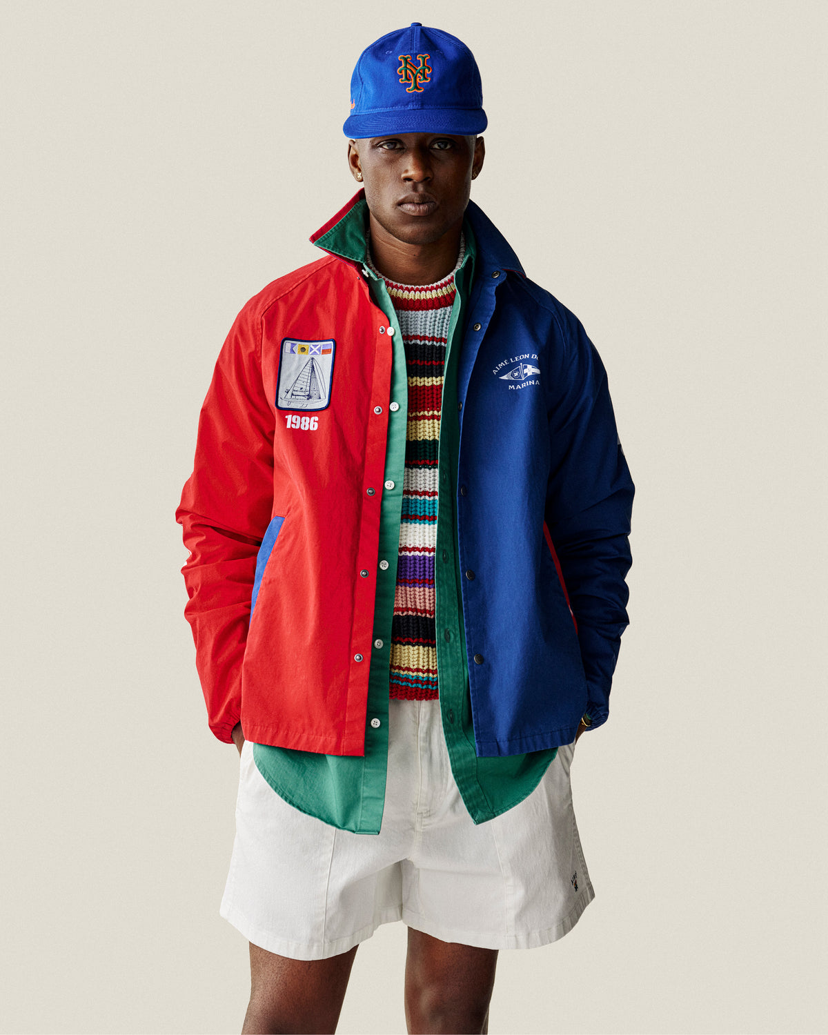 Man in the Leon Overshirt, striped sweater, white shorts, and blue Mets cap stands against a light background.