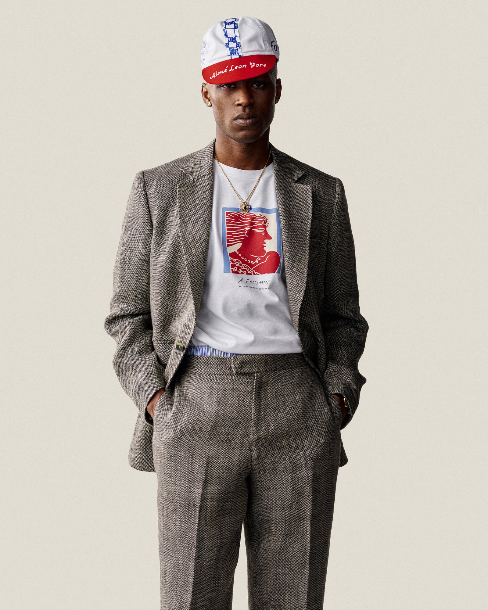 Man in Single-Breasted Yarn Dyed Linen Suit Jacket, white graphic tee, and red-white cap, hands in pockets.