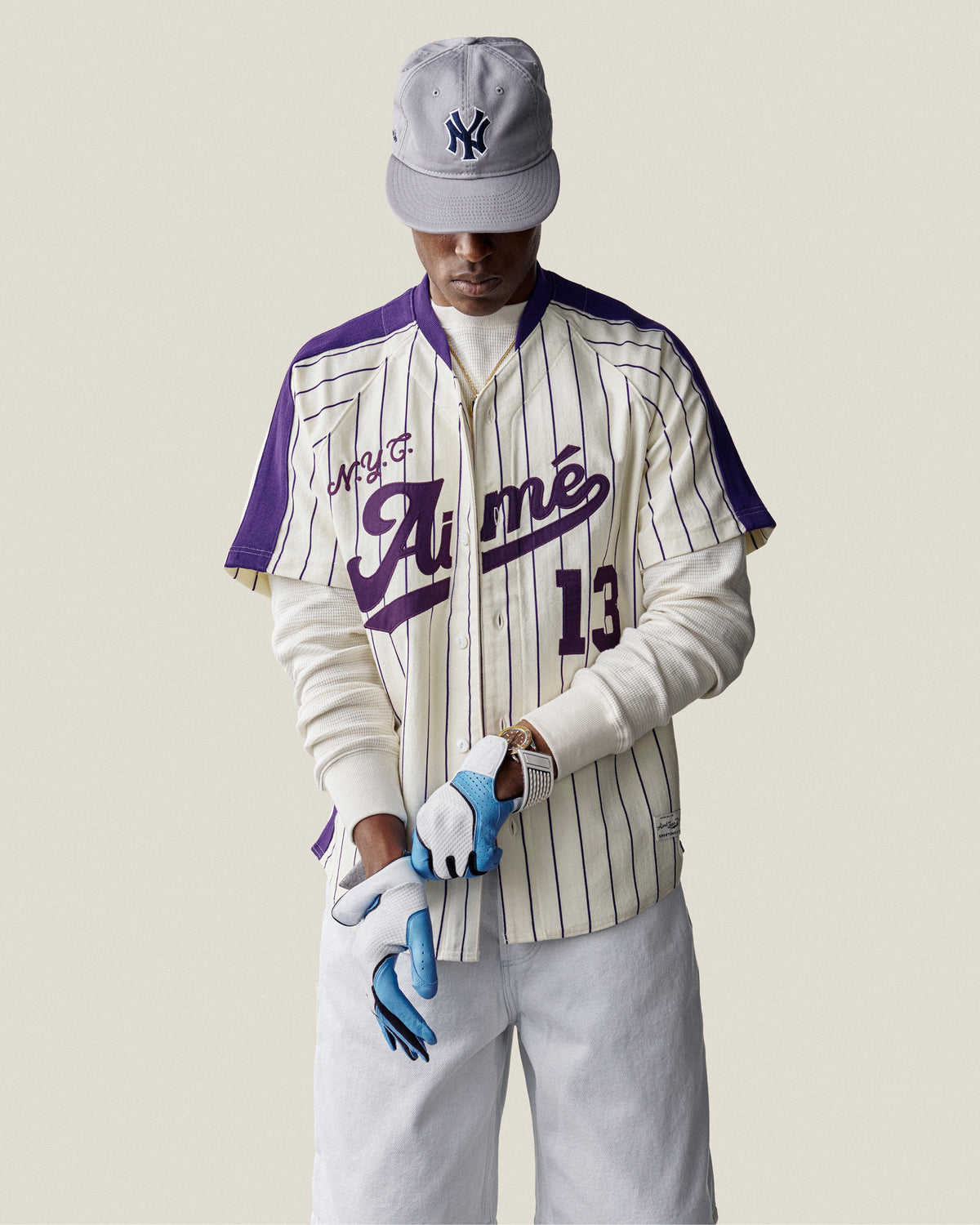 Man wearing a Long-Sleeve Waffle Thermal, gray NY cap, white pants, and blue gloves against a plain background.