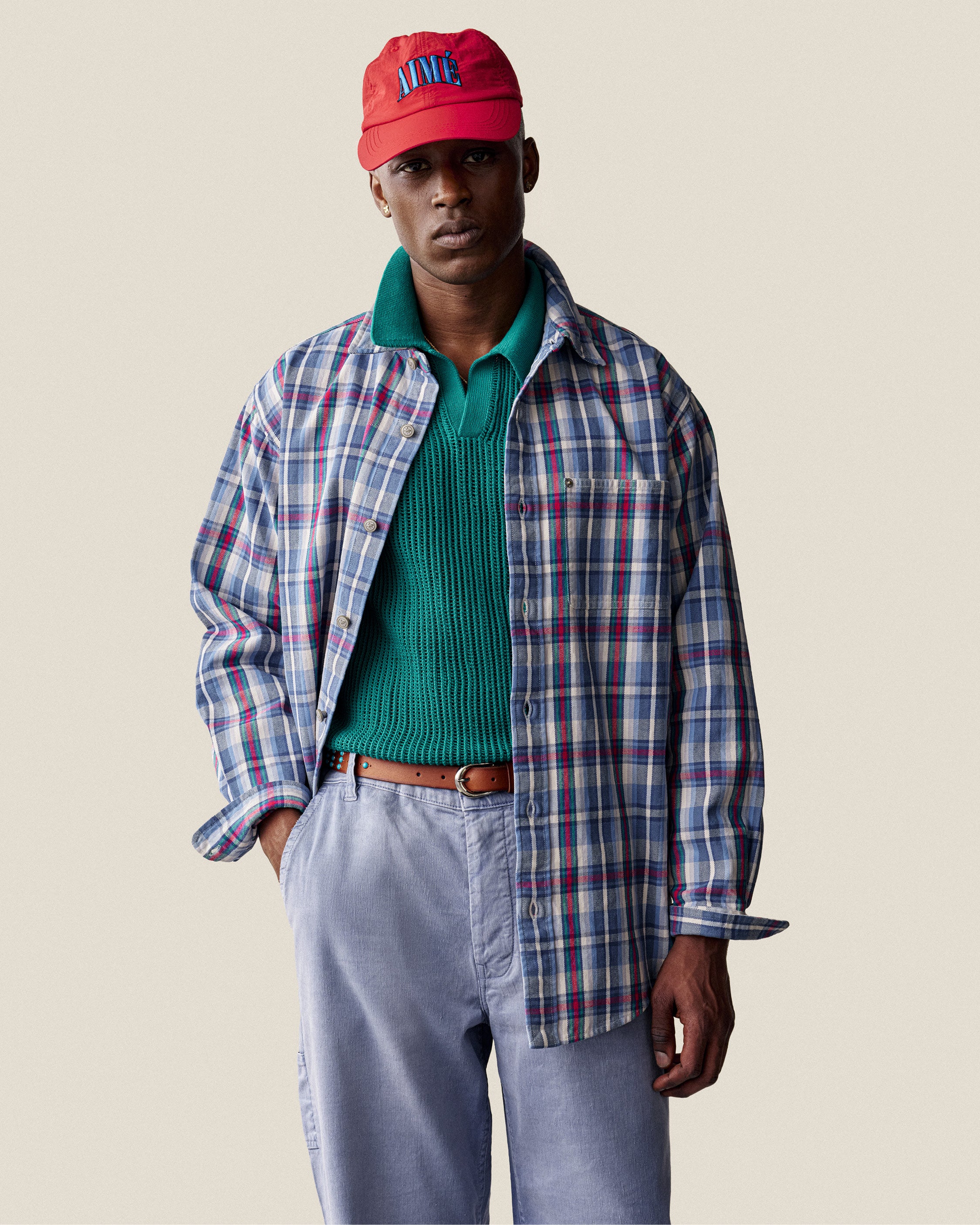 Man wearing a plaid work shirt stands with one hand in his pocket against a plain background.