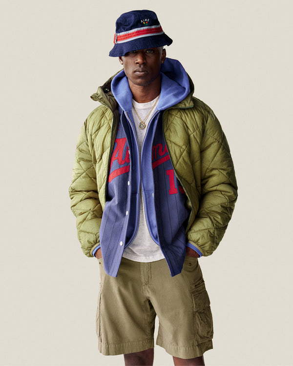 A man wearing a bucket hat, green puffer jacket, Sun Faded Full-Zip Hoodie, sports jersey, and khaki cargo shorts.