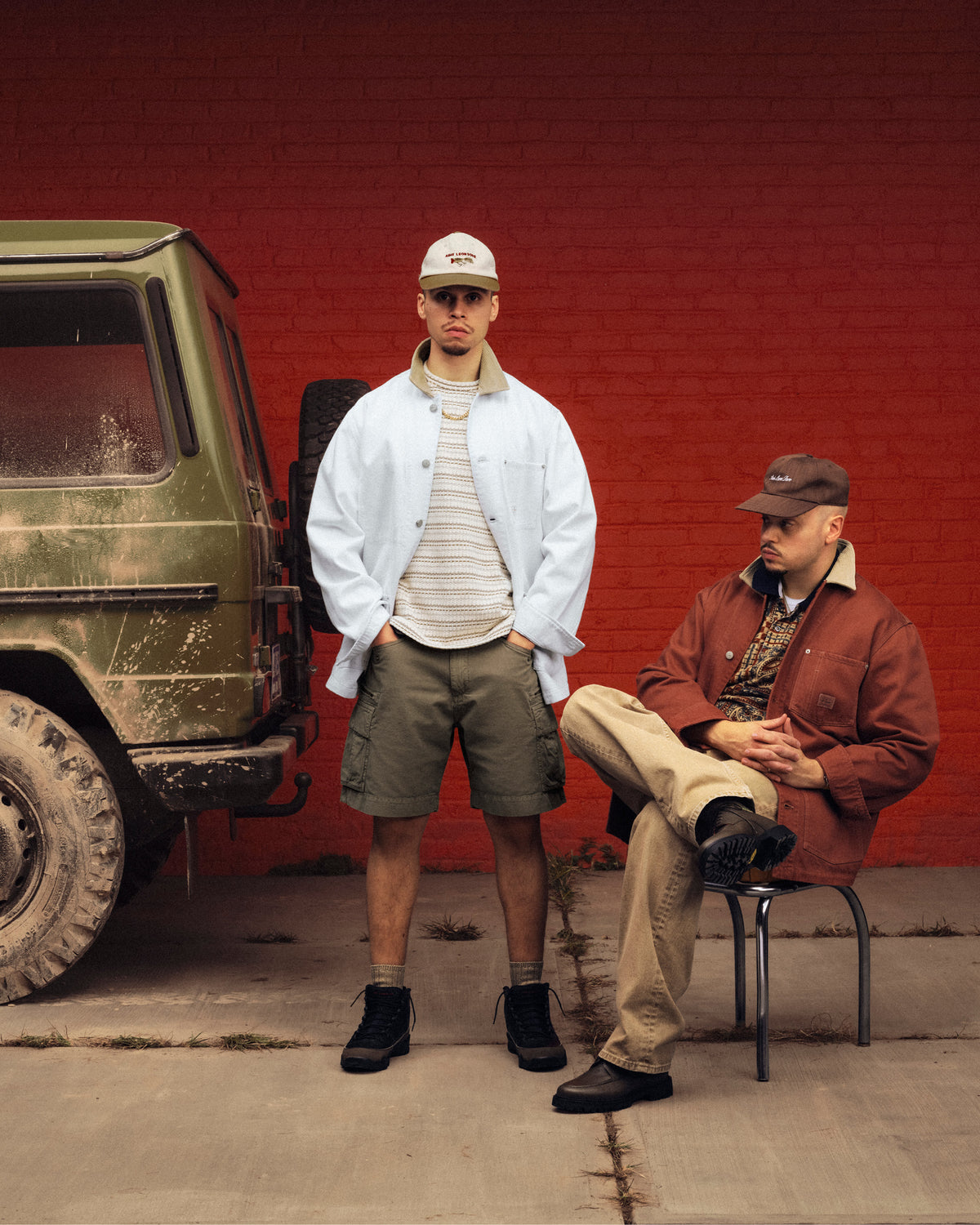 Two men, one standing and one seated, pose by a muddy green SUV; both wear the Denim Barn Jacket.