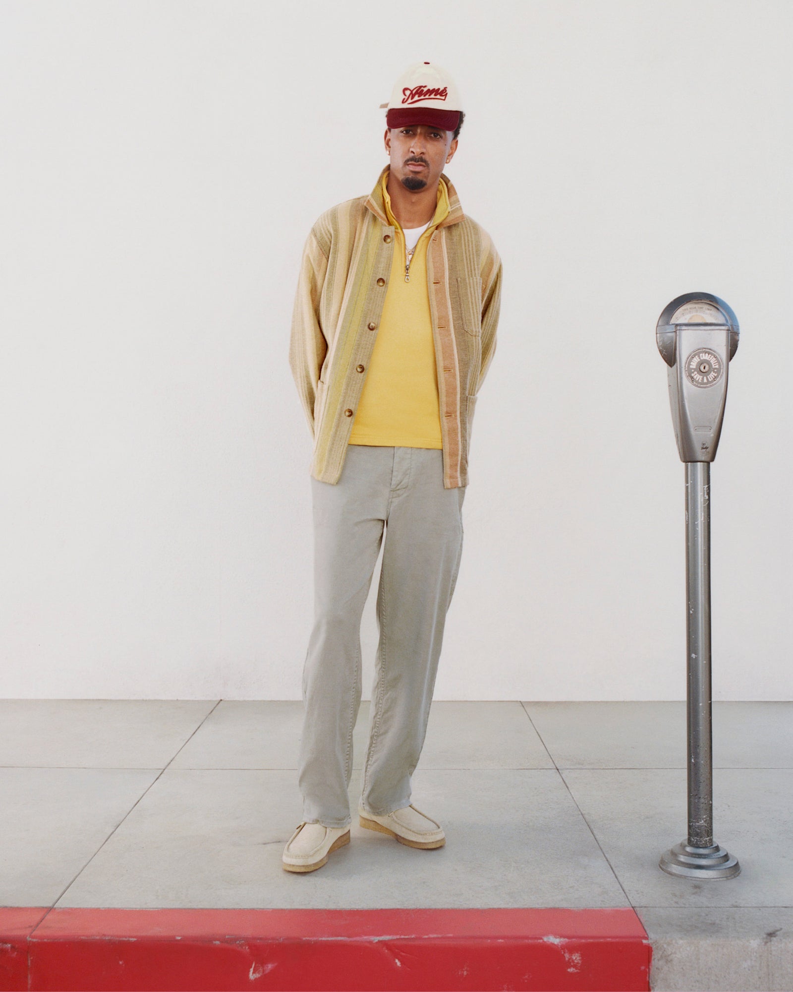 Man in casual clothes and Linen Blend Carpenter Pant stands by a parking meter against a plain white wall.