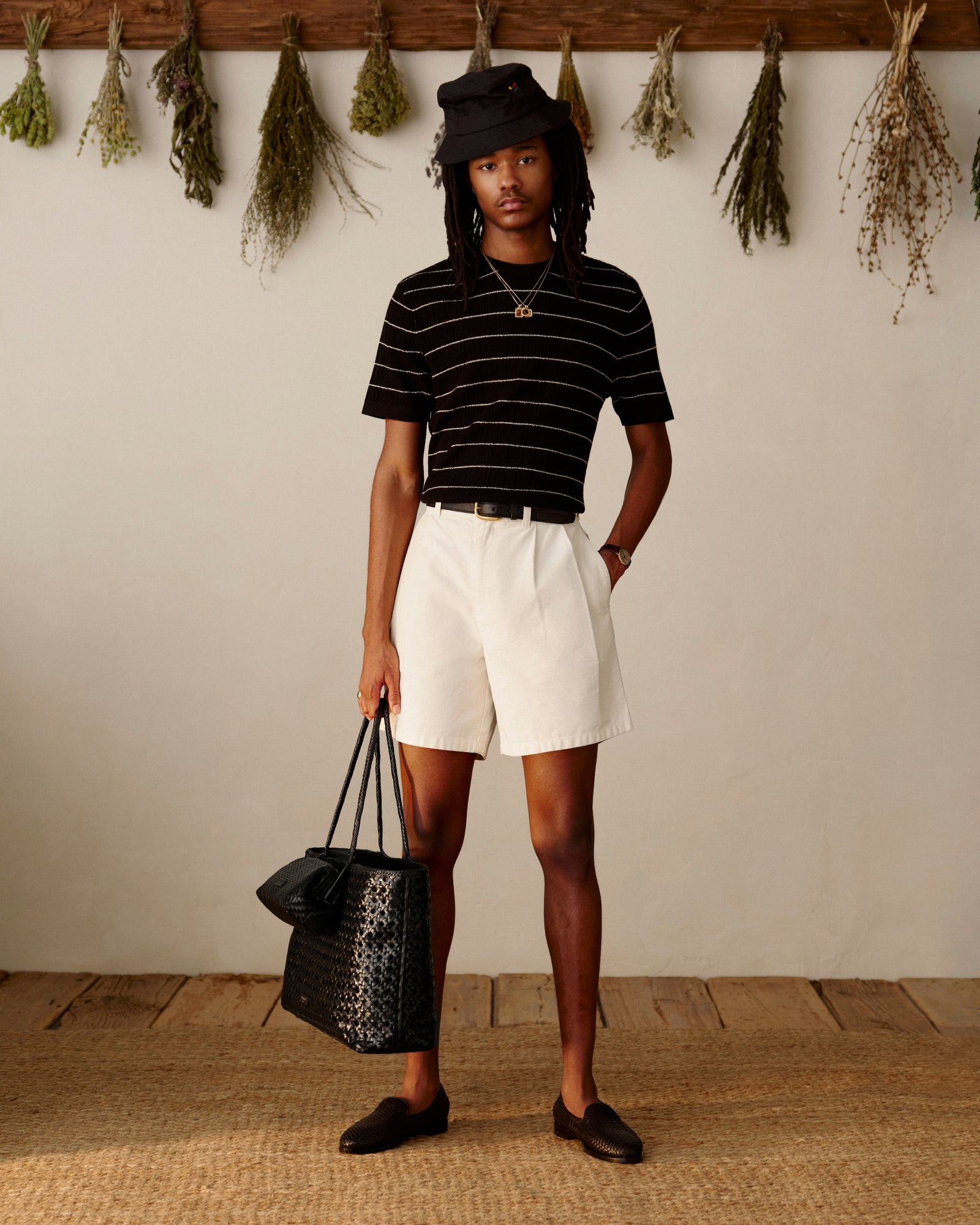 A person in a striped shirt and loafers holds a Woven Leather Shoulder Bag, standing indoors.