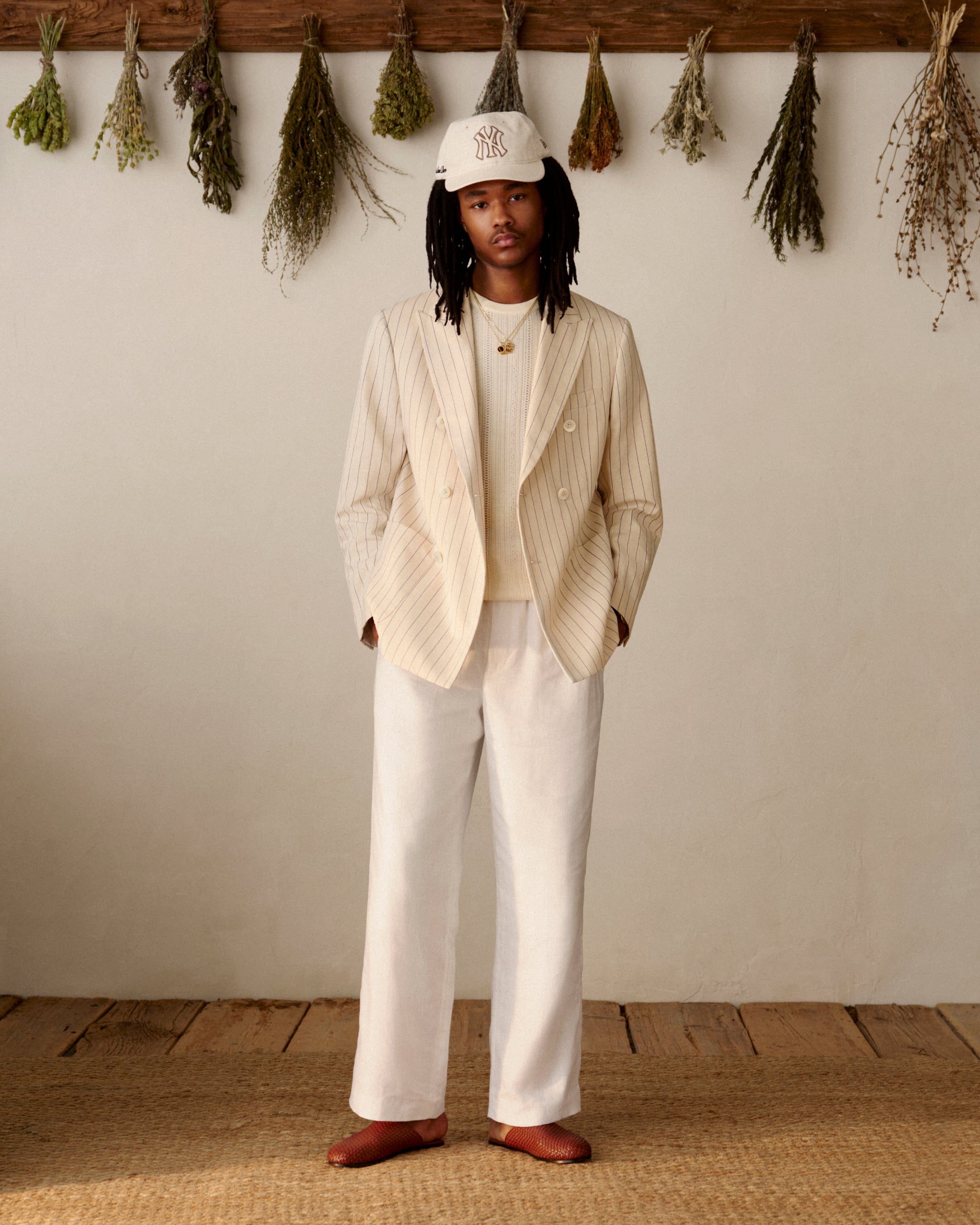 Wearing a cream suit and white shirt, a person indoors sports an ALD / New York Yankees Retro Fit Hat.