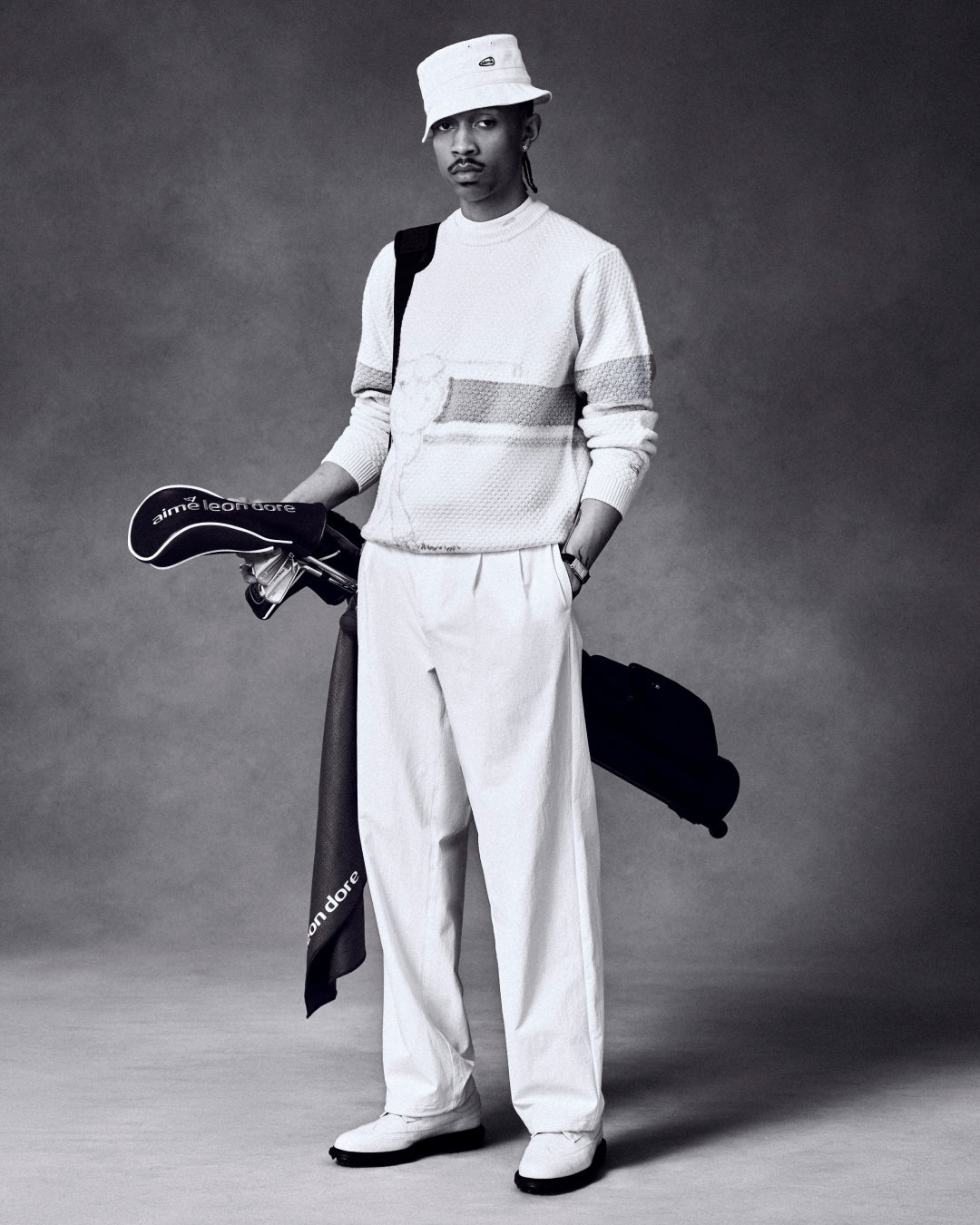 A man in white poses with the ALD Golf Driver Cover and clubs against a dark studio backdrop.