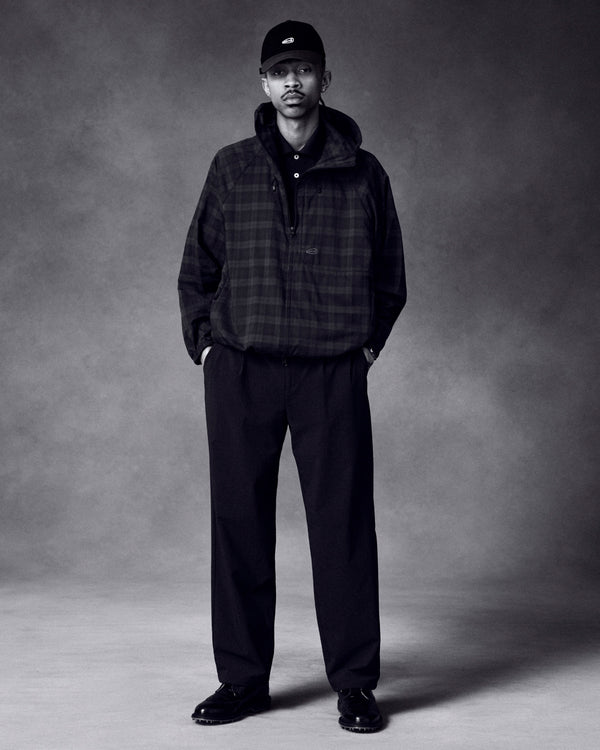 A man stands with hands in pockets, wearing a plaid jacket, wide-leg pants, ALD Golf Logo Hat, and black shoes.