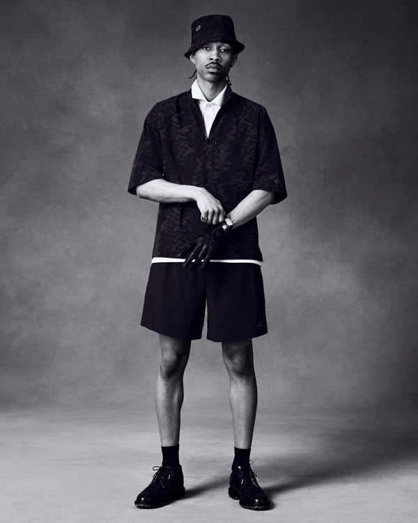 A man in ALD Golf Performance Short, bucket hat, dark shirt, gloves, and dress shoes stands against a plain background.