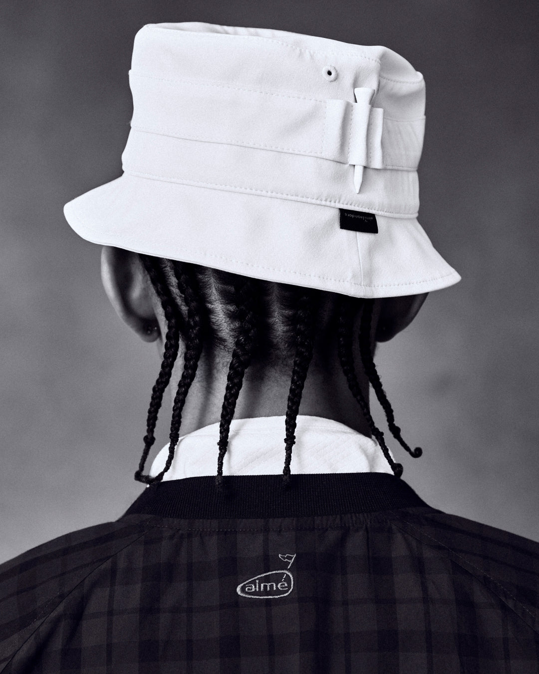 Person with braided hair in an ALD Golf Bucket Hat and dark jacket, shown from behind against a plain background.