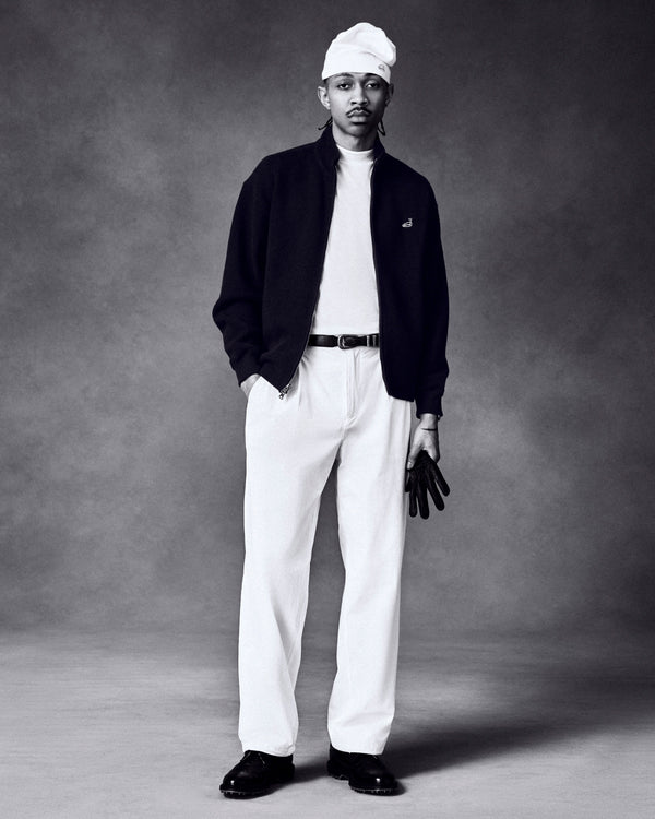 A man in a white hat, white shirt, pants, and dark jacket holds an ALD / FootJoy StaSof Heritage Glove (Left).