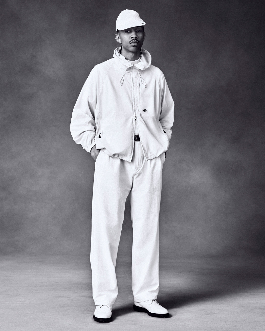 Man wears the ALD Golf Lightweight Tips Windbreaker, pants, cap, and shoes against a dark background.