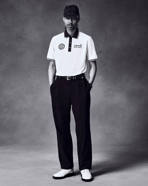A man wears ALD Golf Cordura Double Pleated Pant with a polo and cap, hands in pockets, against a plain backdrop.
