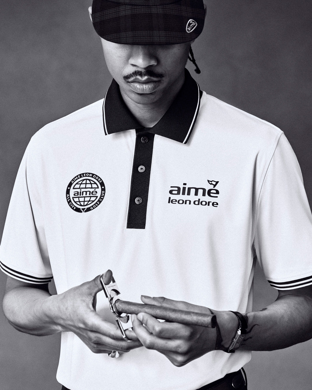 Black and white photo of a man in an ALD Golf Tour Polo, looking down and holding a watch.