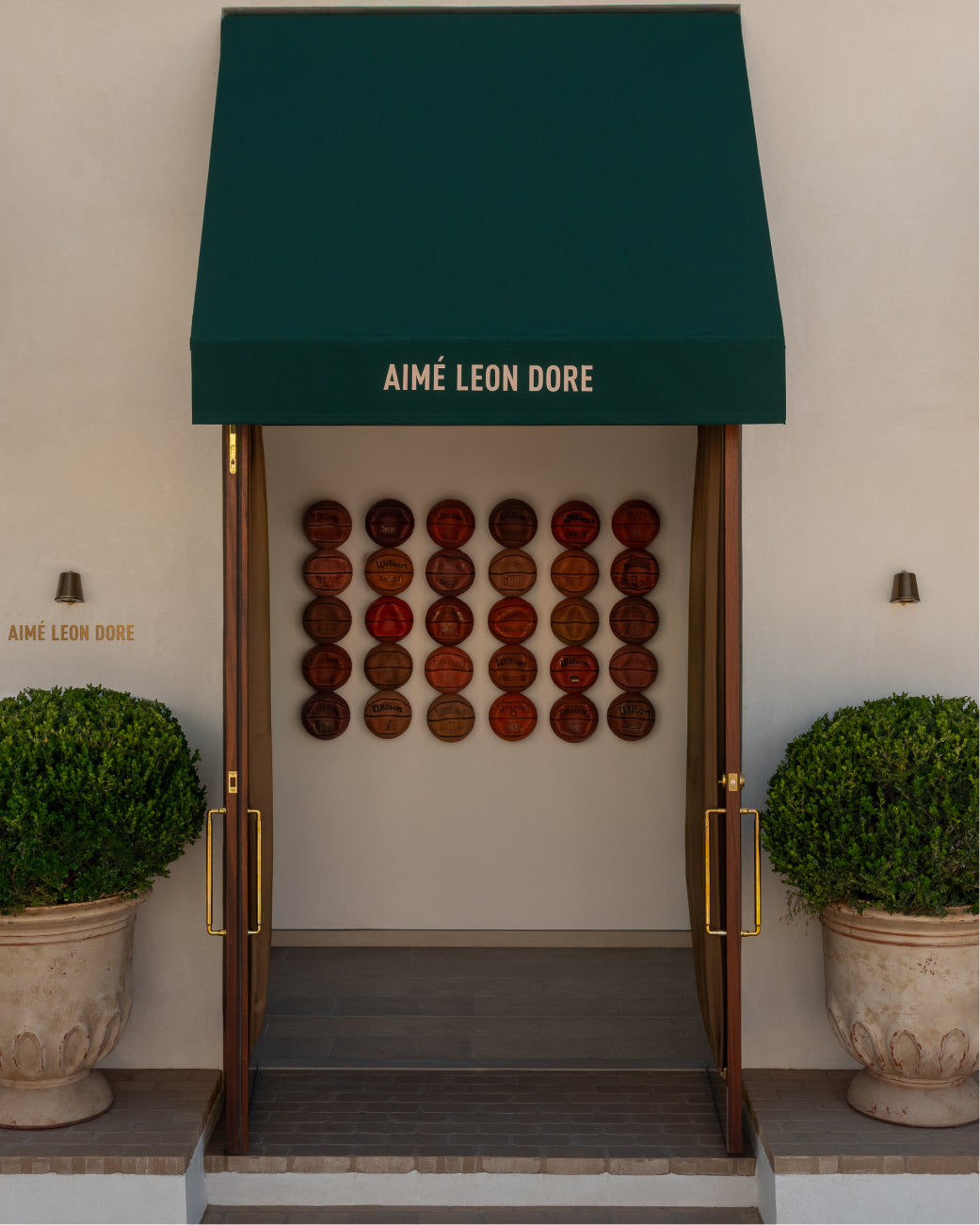 Aime Leon Dore store entrance in Los Angeles with green awning and decorative wall.