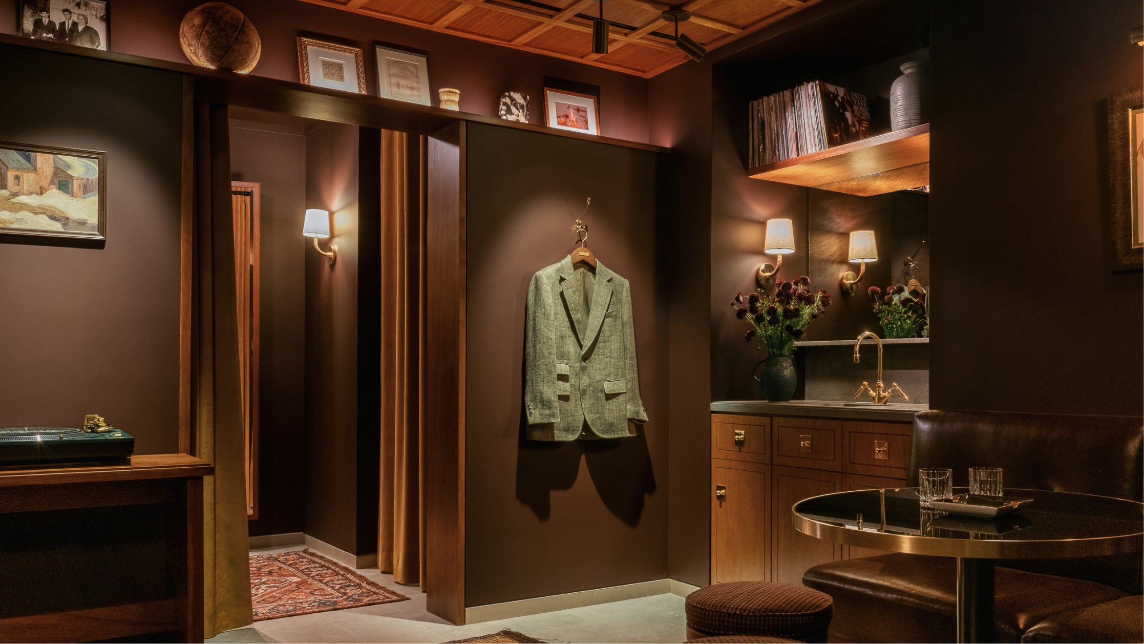 Green suit jacket hanging on a hook in a dimly lit room with wooden paneling and decor at Los Angeles flagship store