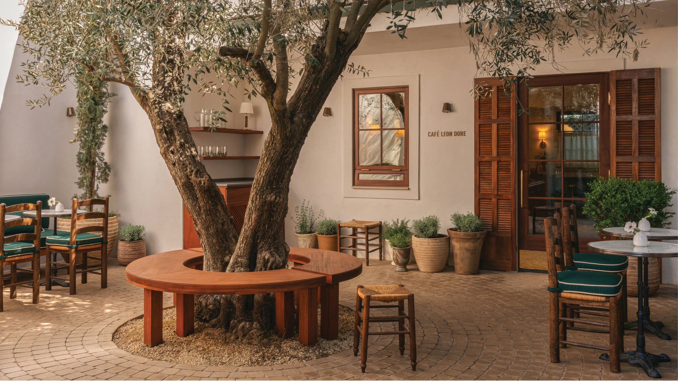 Outdoor seating area with tables, chairs, and a large tree in a courtyard setting.