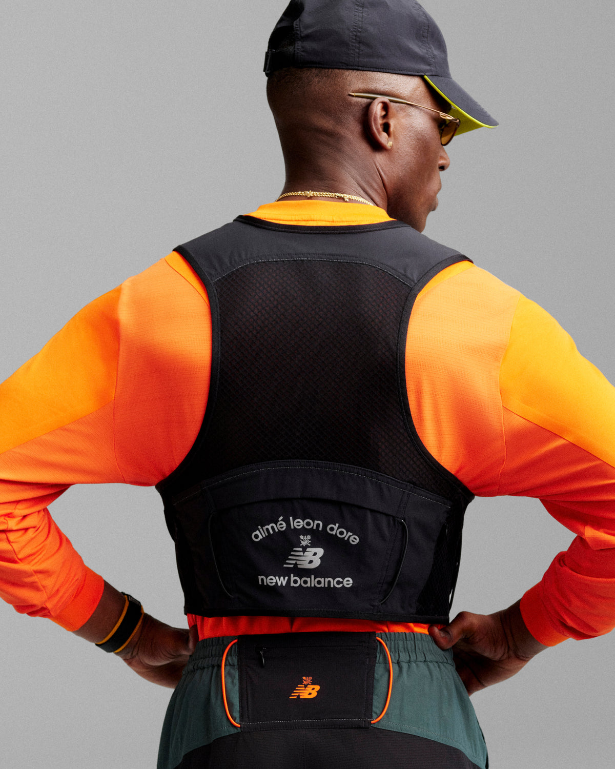 Man in orange shirt and black cap wears an ALD / New Balance Hydrovest, facing away from the camera.