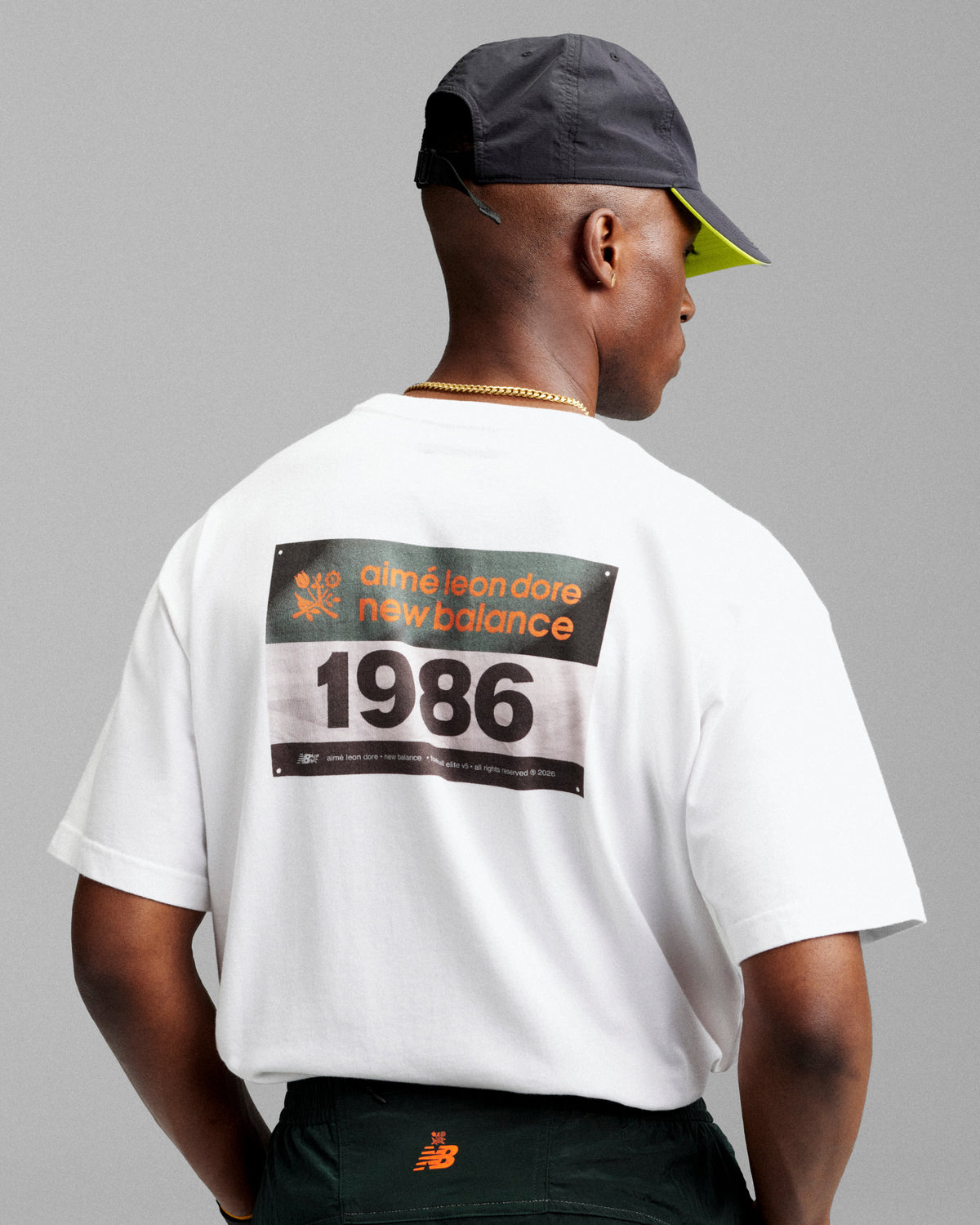 Man in a white ALD / New Balance Running Bib Tee and dark cap, facing away from the camera.