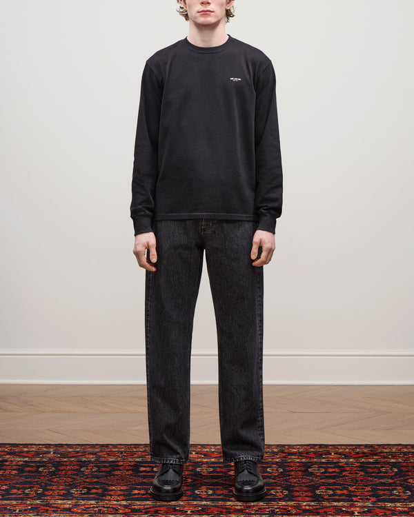 Person standing on a patterned rug wearing the Long-Sleeve Micro Logo Tee, black jeans, and black shoes.