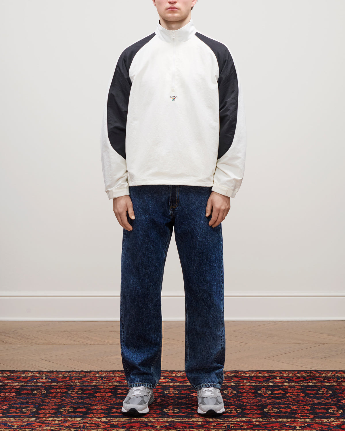 Person wearing the Crest Nylon Half-Zip Pullover, blue jeans, and gray sneakers standing on a patterned rug.