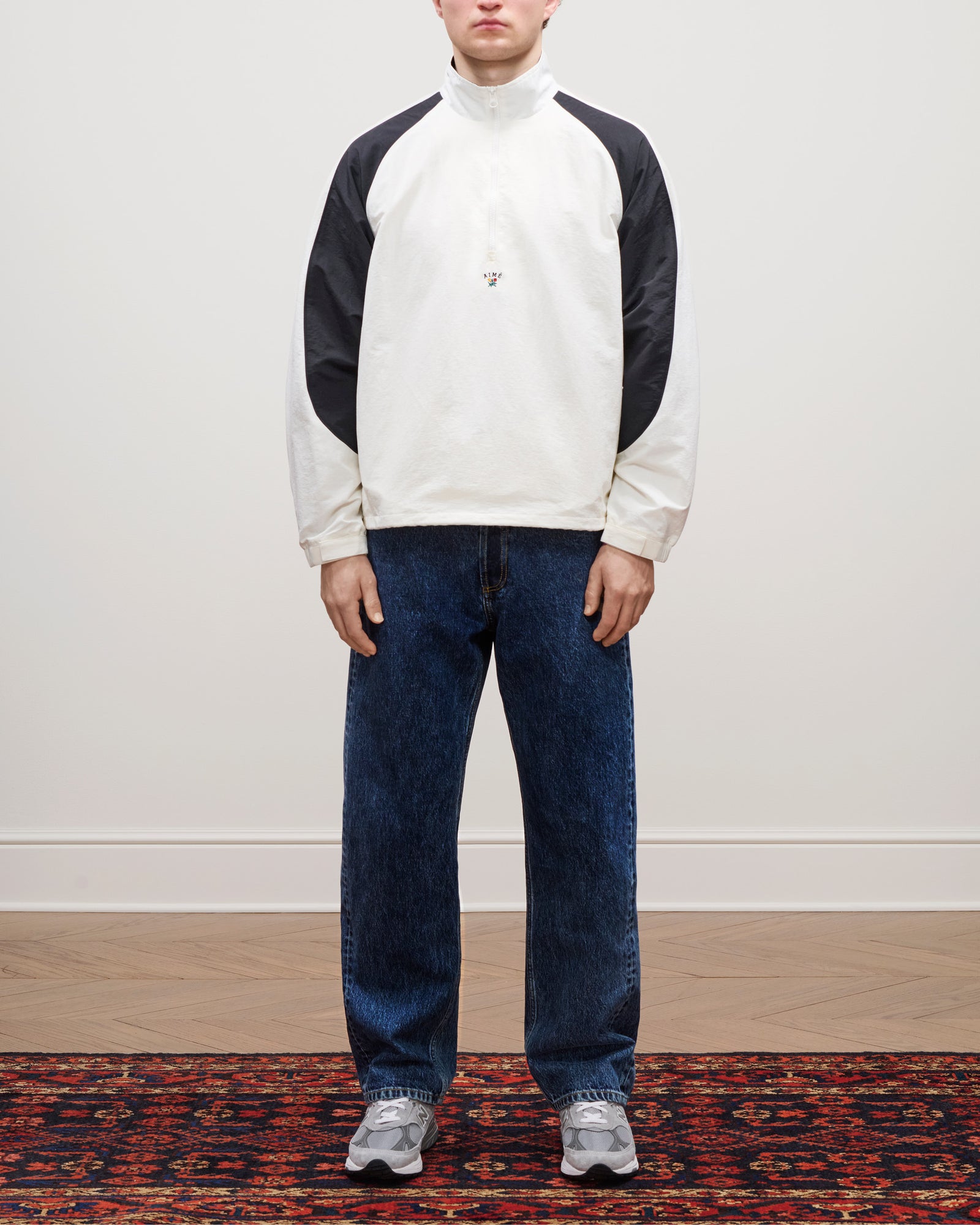 Person wearing the Crest Nylon Half-Zip Pullover, blue jeans, and gray sneakers standing on a patterned rug.