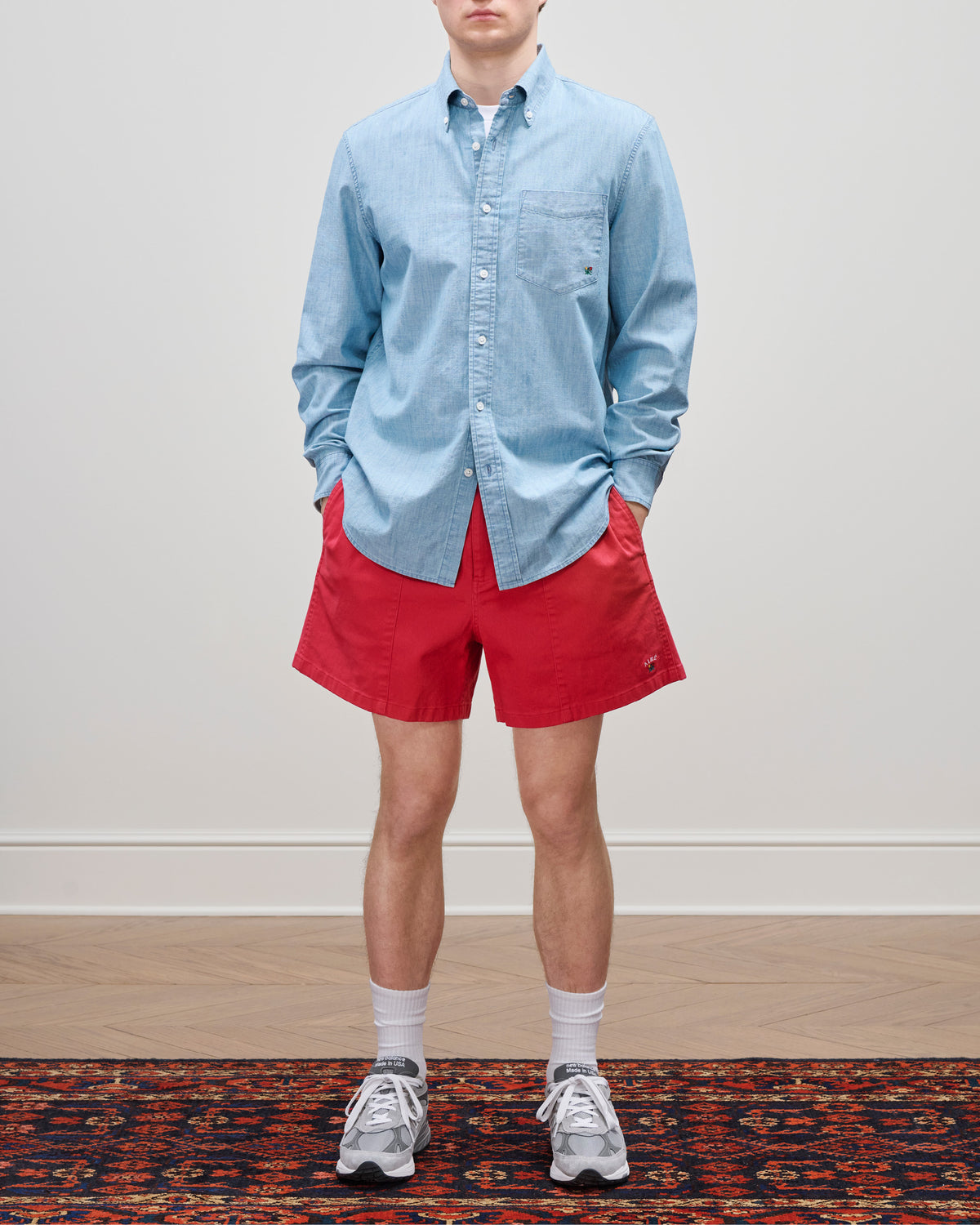 Person wears Crest Casual Short, light blue shirt, white socks, gray sneakers, standing on a patterned rug.