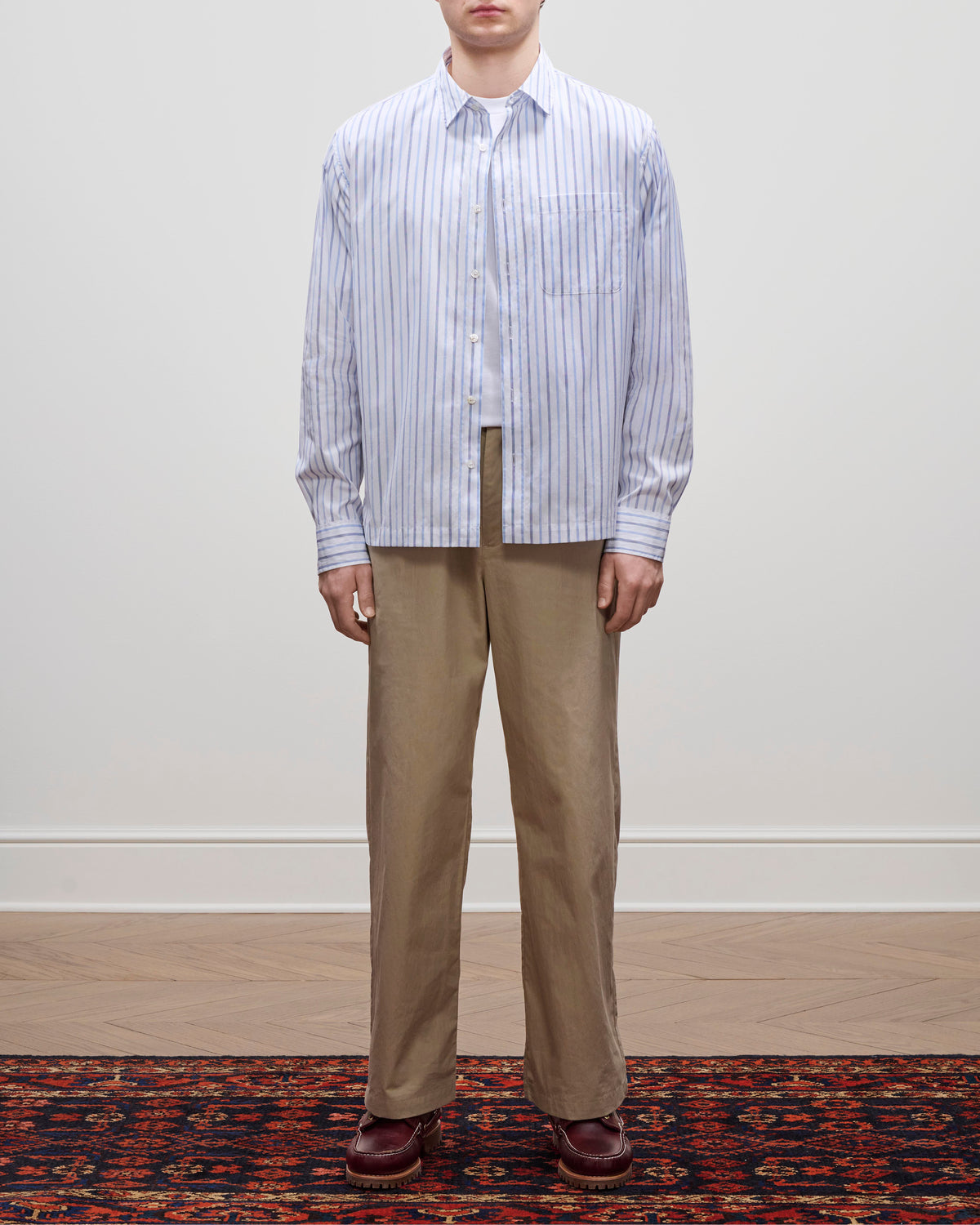 A person stands on a patterned rug wearing tan pants, brown shoes, and the Poplin Casual Shirt against a plain background.