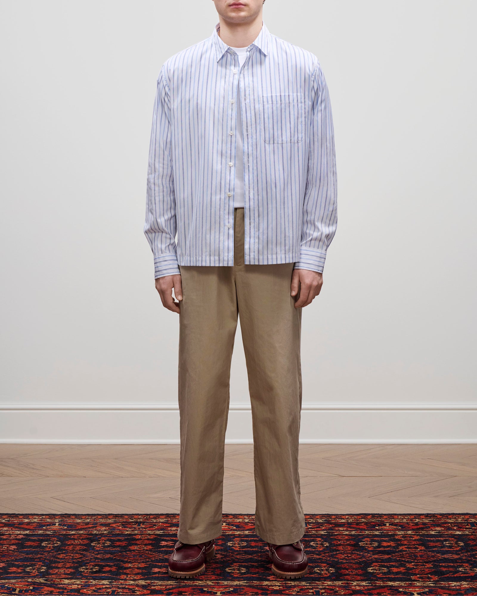 A person stands on a patterned rug wearing tan pants, brown shoes, and the Poplin Casual Shirt against a plain background.
