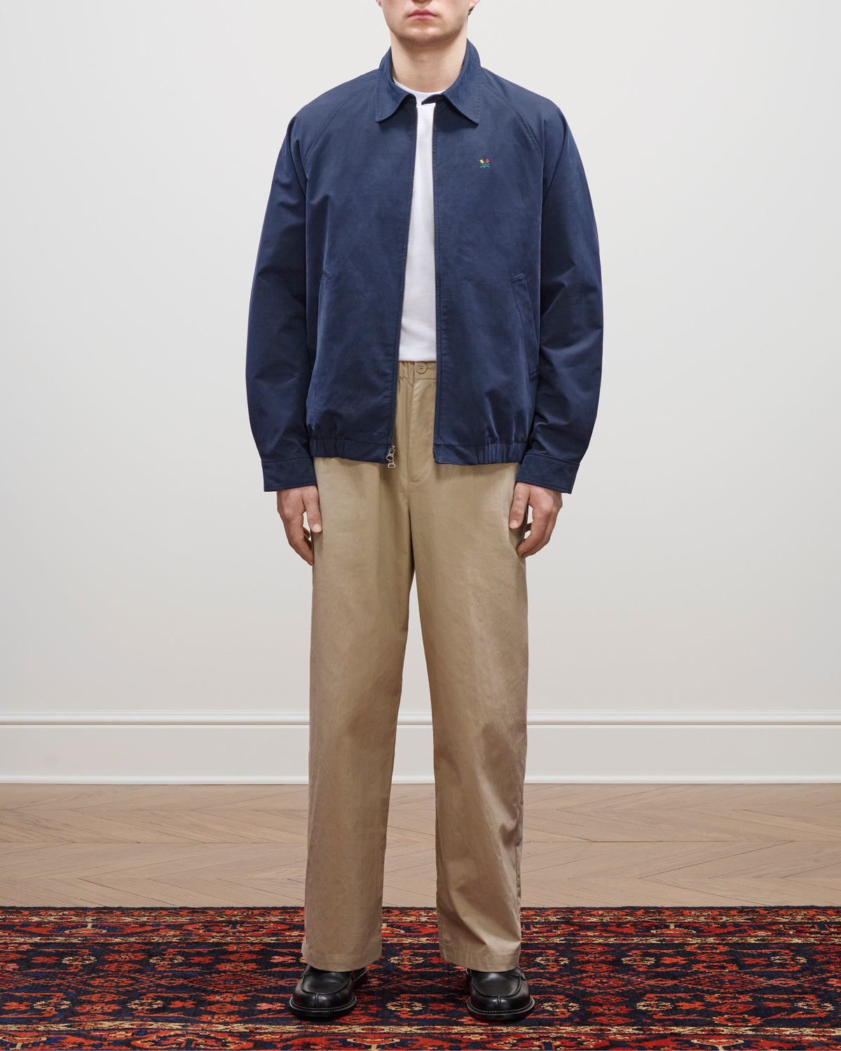 A person in the Crest Casual Jacket, white shirt, beige pants, and black shoes stands on a patterned rug.