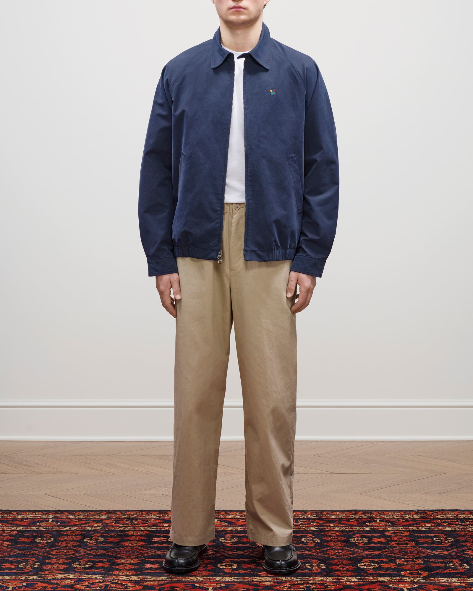 A person in the Crest Casual Jacket, white shirt, beige pants, and black shoes stands on a patterned rug.