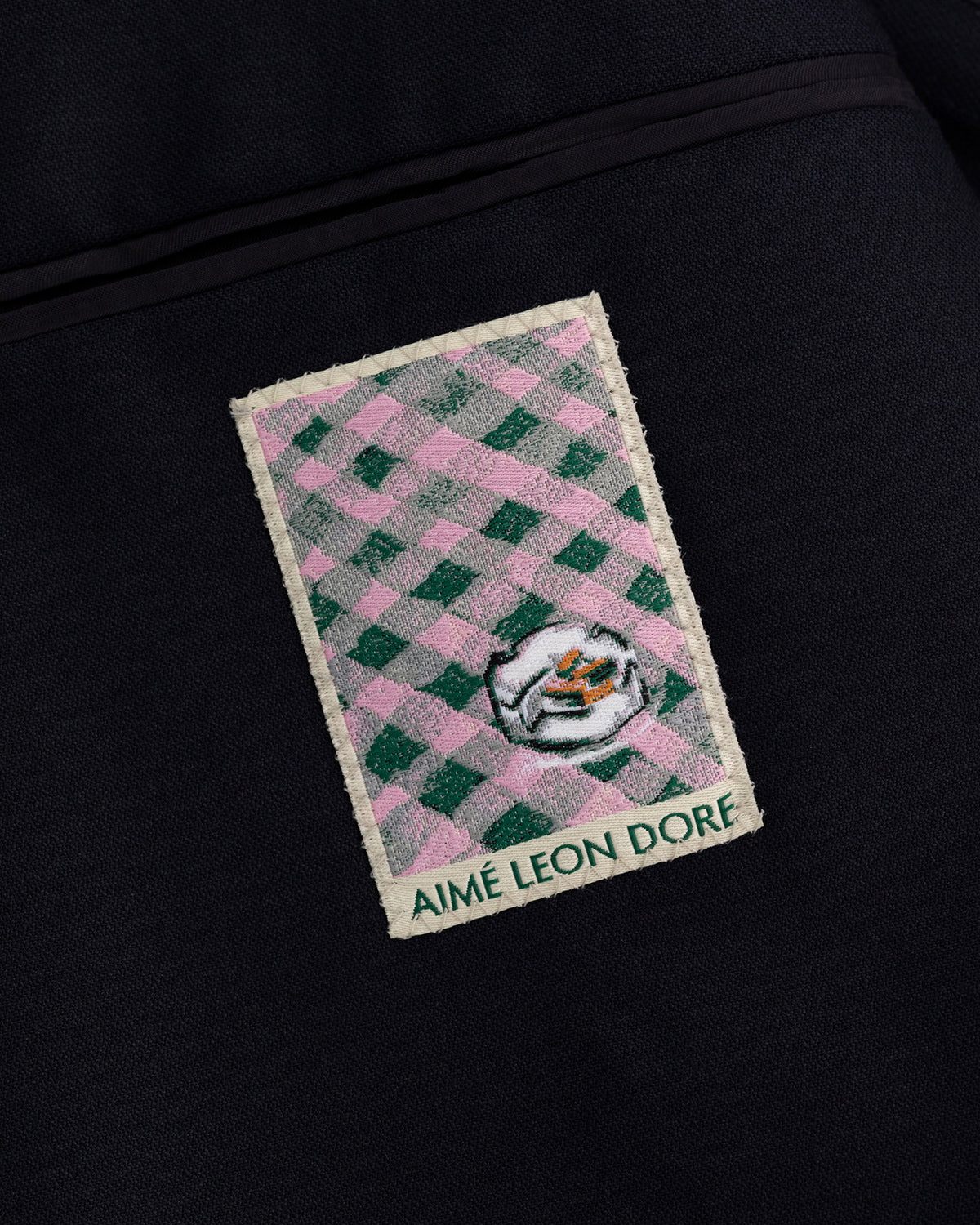 A patch with a green and pink check, small face, and “AIMÉ LEON DORE” on the Tropical Wool Suit Jacket.