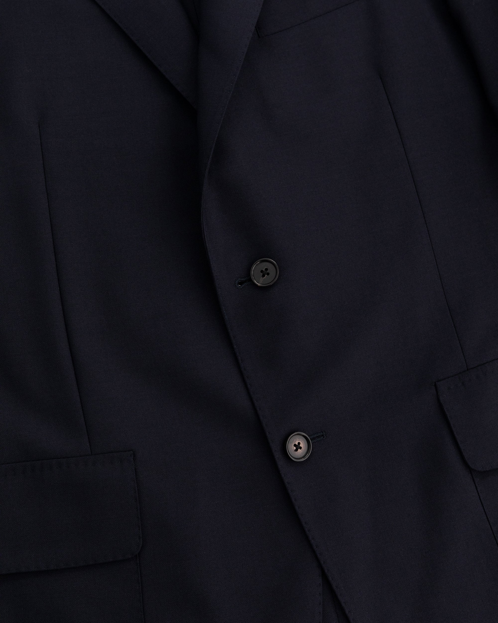 Close-up of the Tropical Wool Suit Jacket in dark navy with two black buttons and front flap pockets.