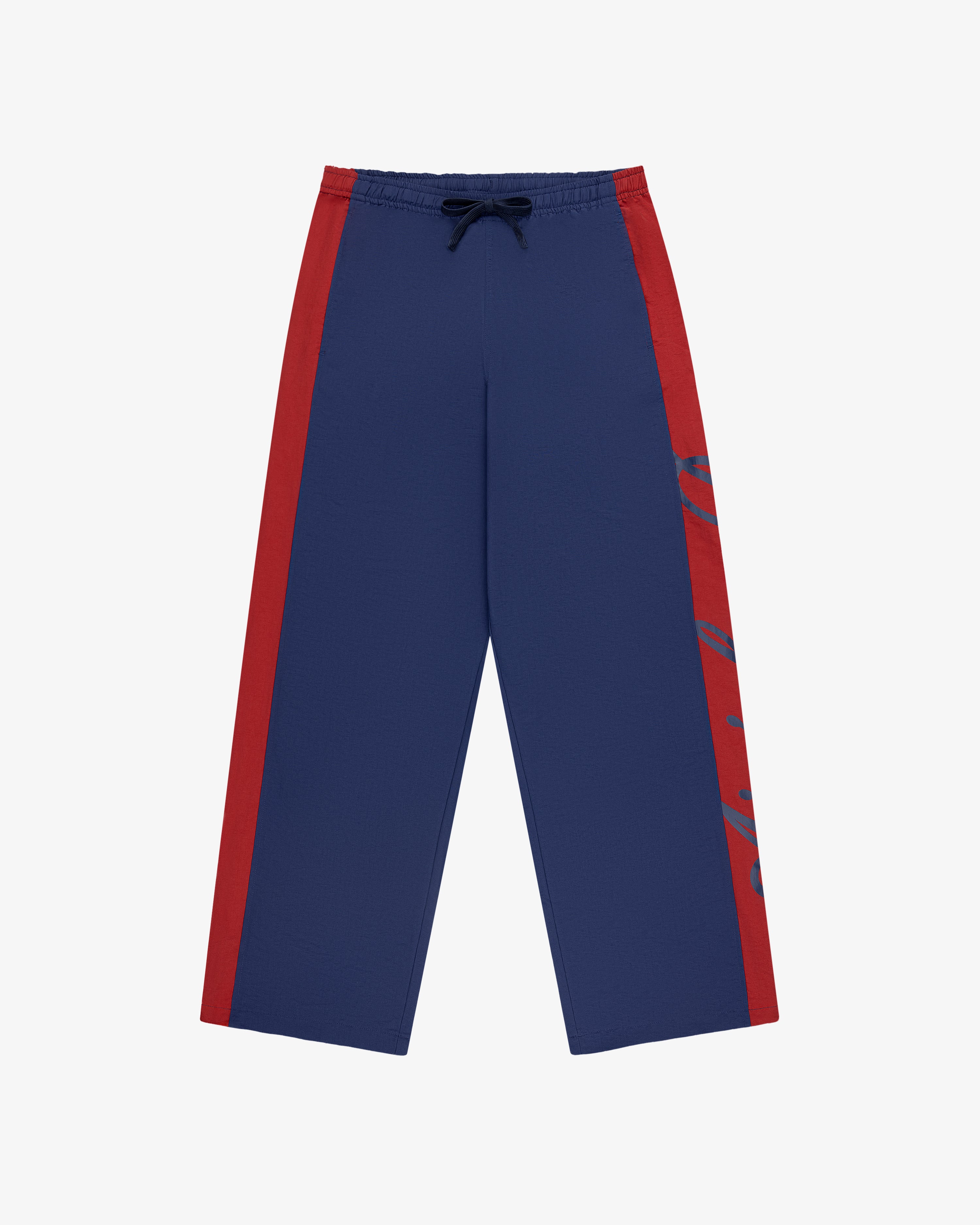 Colorblock Track Pant: blue wide-leg style with red side stripes, drawstring waist, and subtle graphic on one leg.