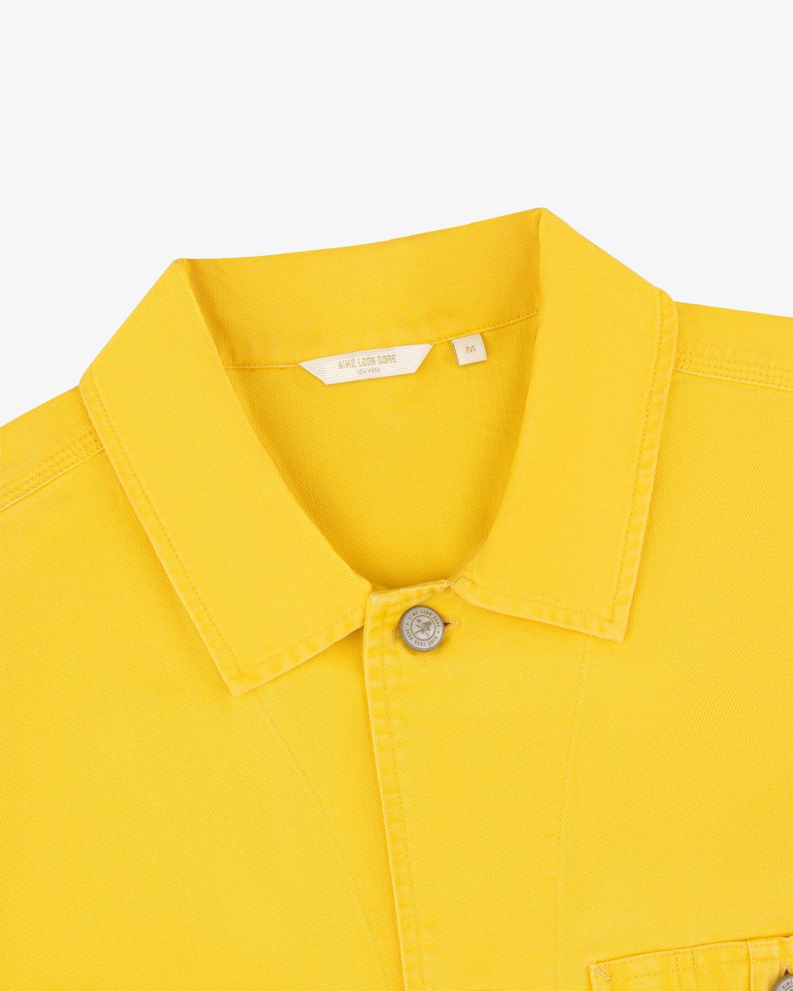 Carpenter Overshirt in yellow with collar, one visible button, and white size tag on plain background.