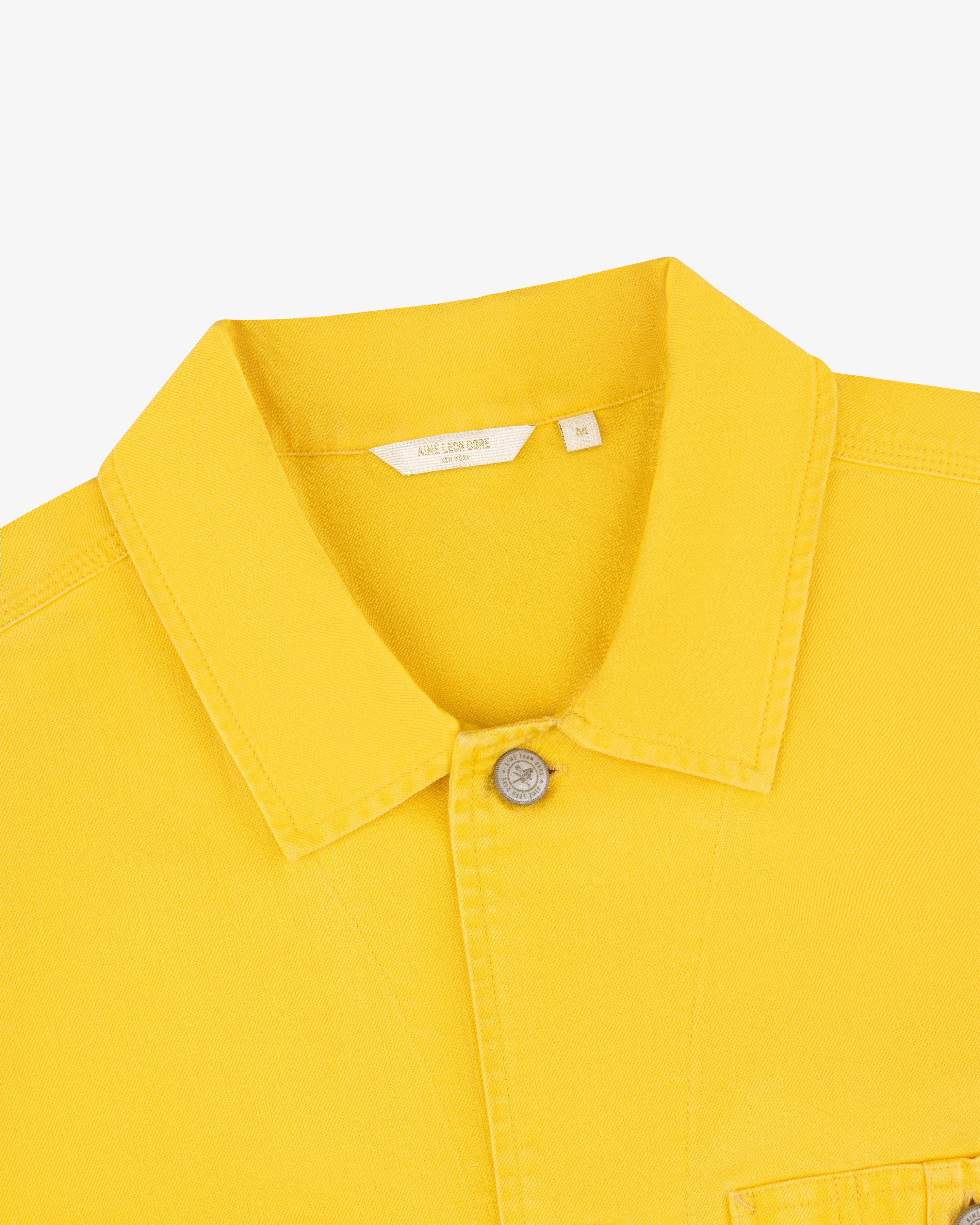 Carpenter Overshirt in yellow with collar, one visible button, and white size tag on plain background.