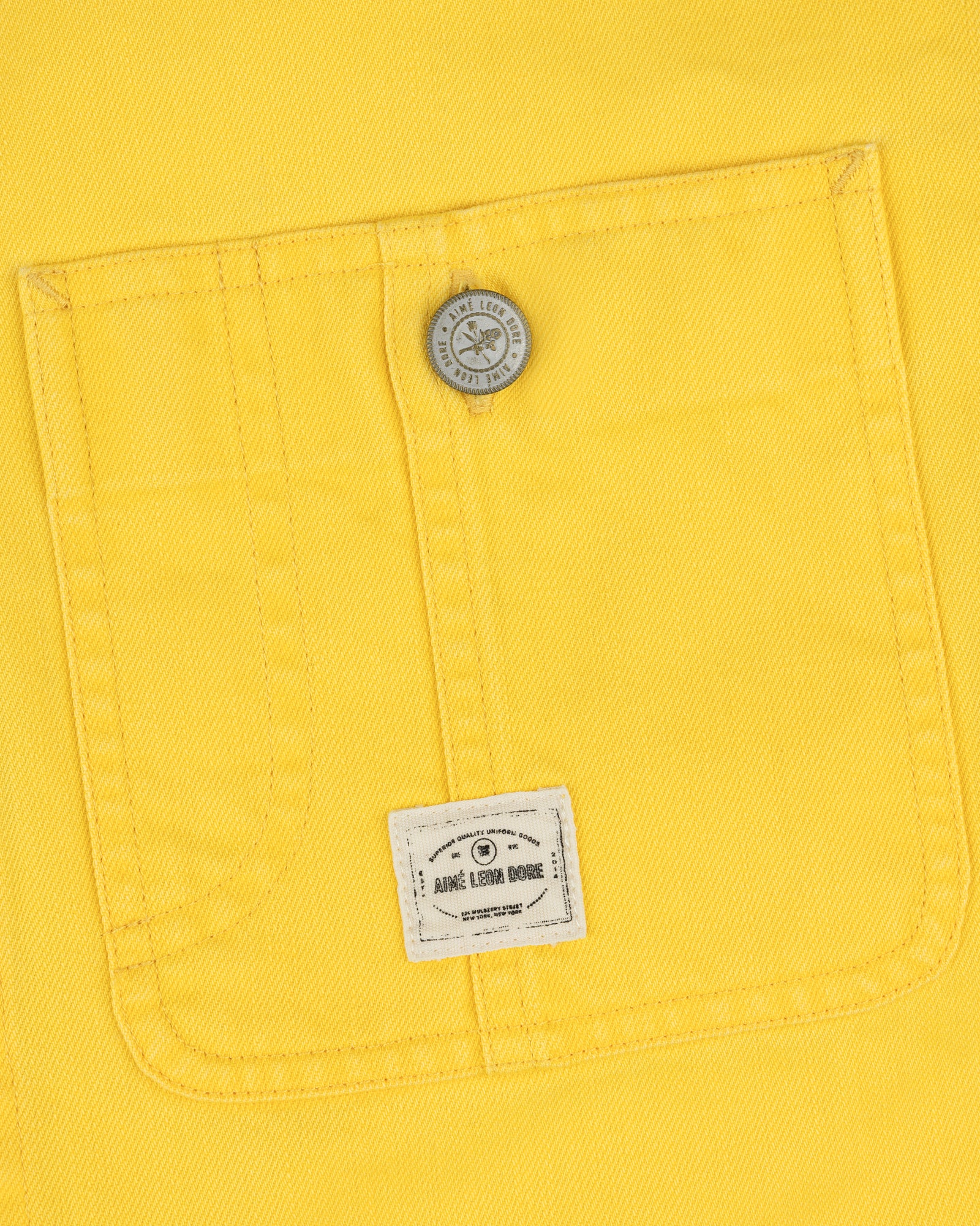 Yellow fabric pocket with a button and small white label on the Carpenter Overshirt’s lower pocket center.