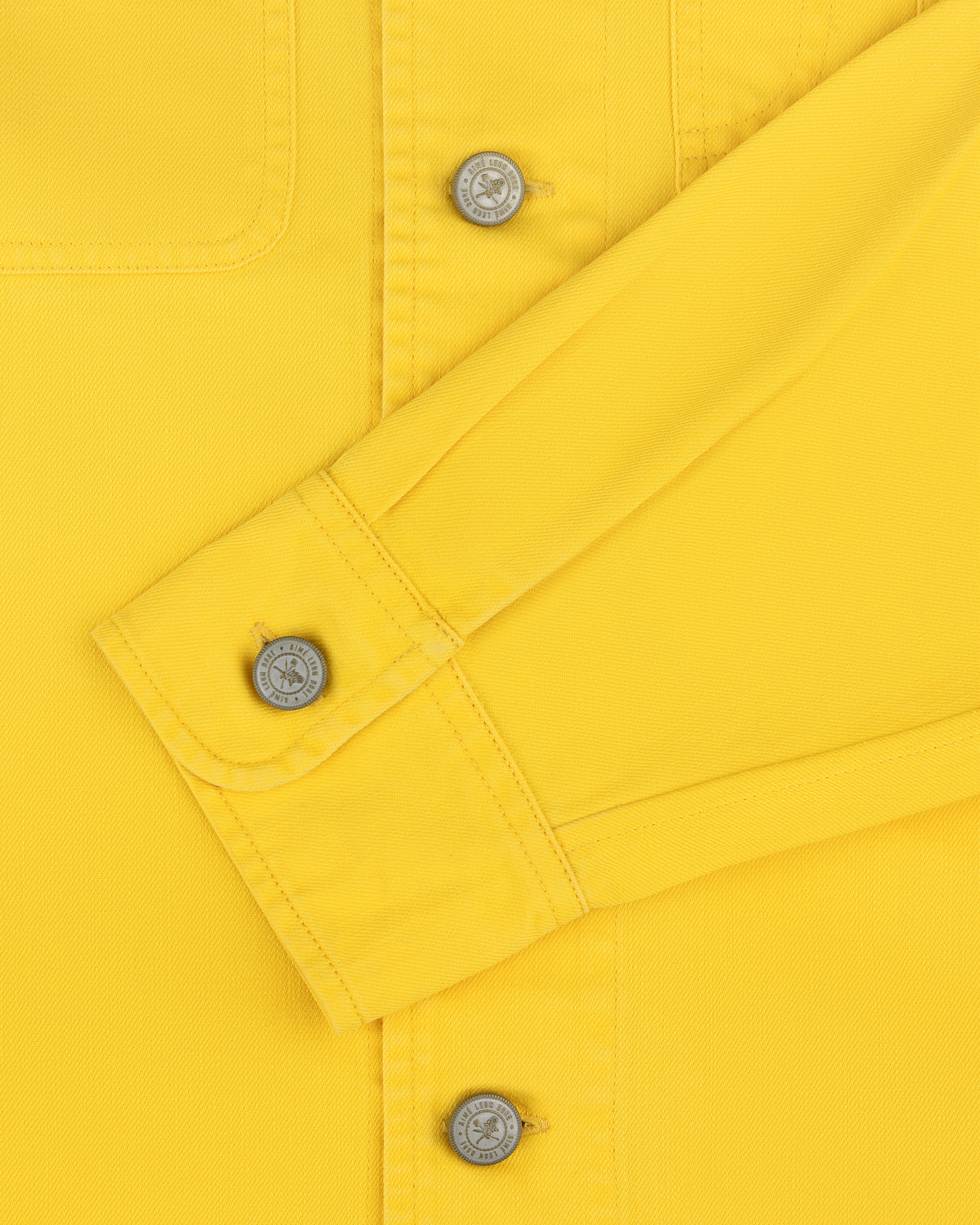 Close-up of the Carpenter Overshirt in yellow with silver buttons and a folded sleeve on a plain background.