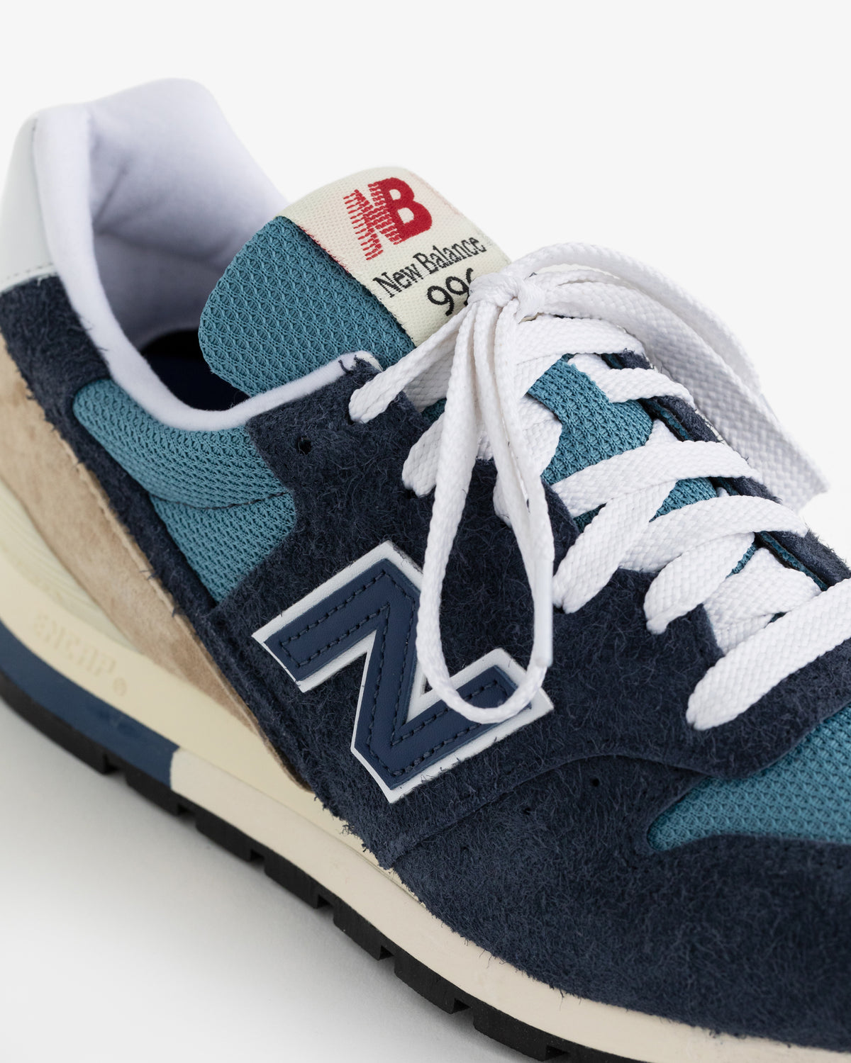 Close-up of a New Balance Made in USA 996 sneaker in navy, light blue, cream, and white with white laces.