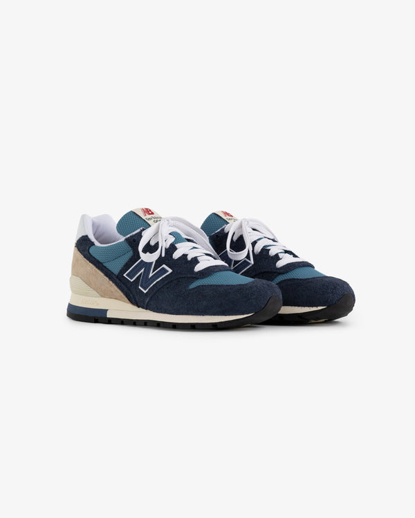 A pair of blue and beige New Balance Made in USA 996 sneakers with white laces on a white background.