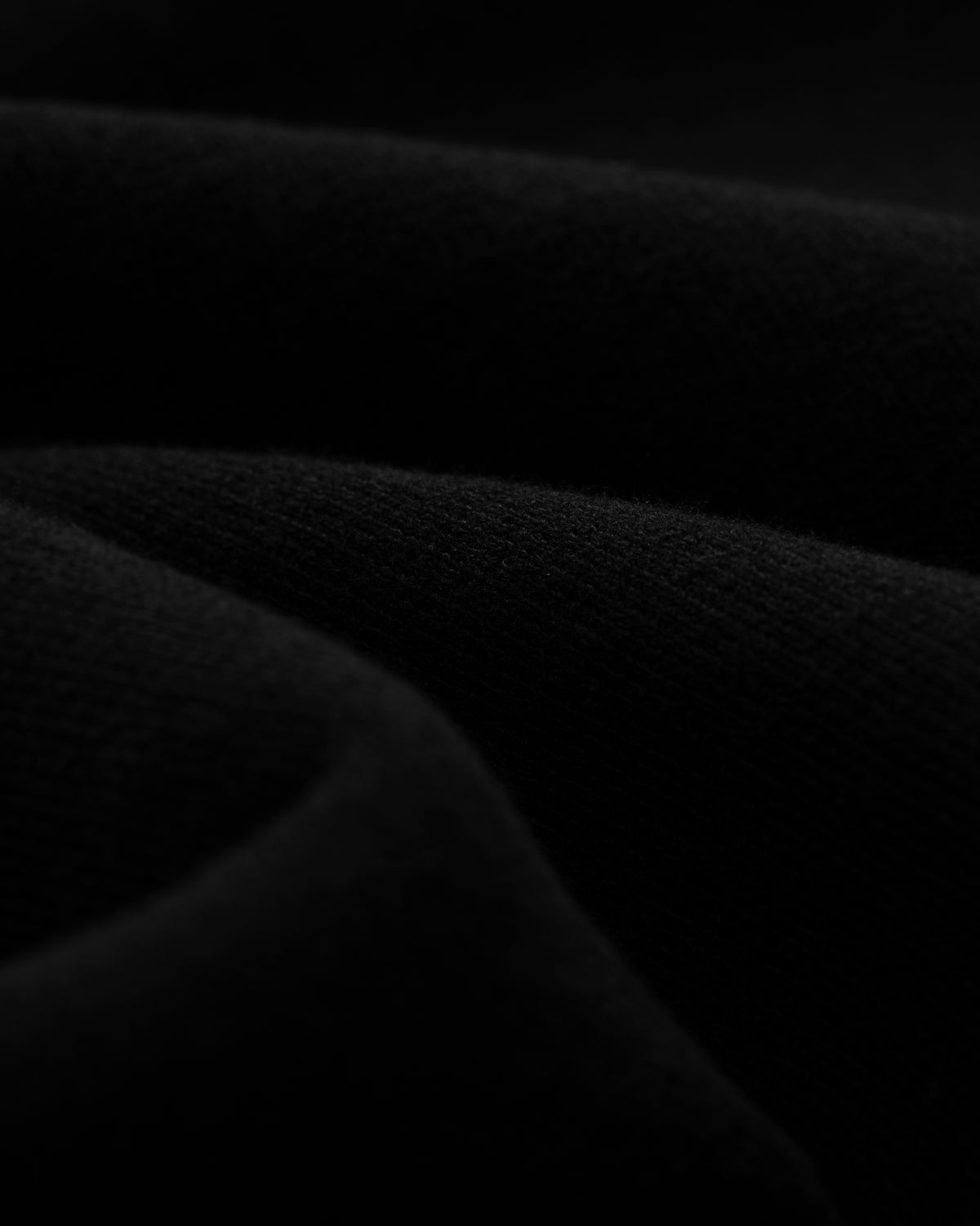Close-up of Tonal Logo Sweatshorts, black folded fabric with a soft texture and gentle curved lines in low light.