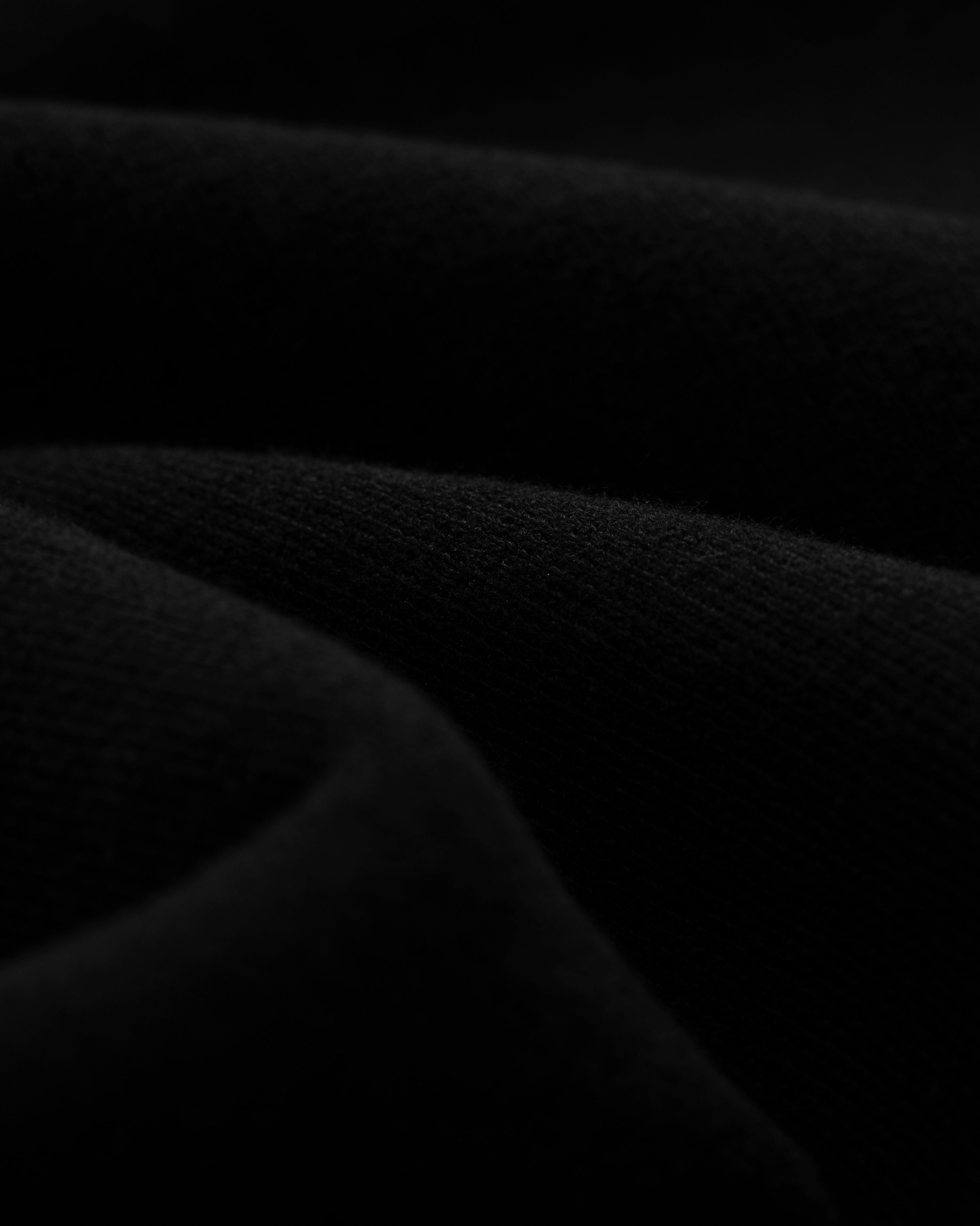 Close-up of Tonal Logo Sweatshorts, black folded fabric with a soft texture and gentle curved lines in low light.
